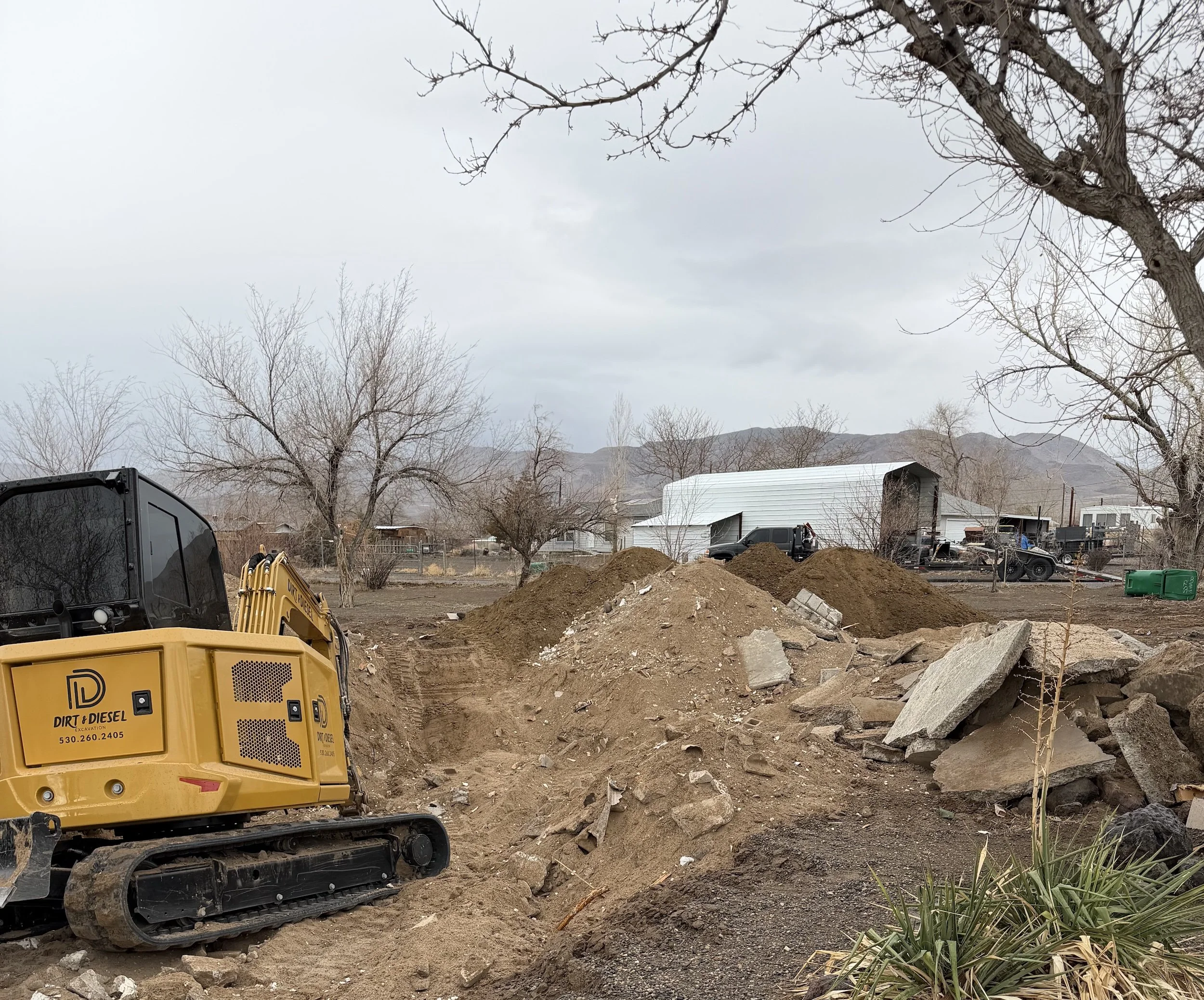 Excavator on a dirt site beside a manufactured hom