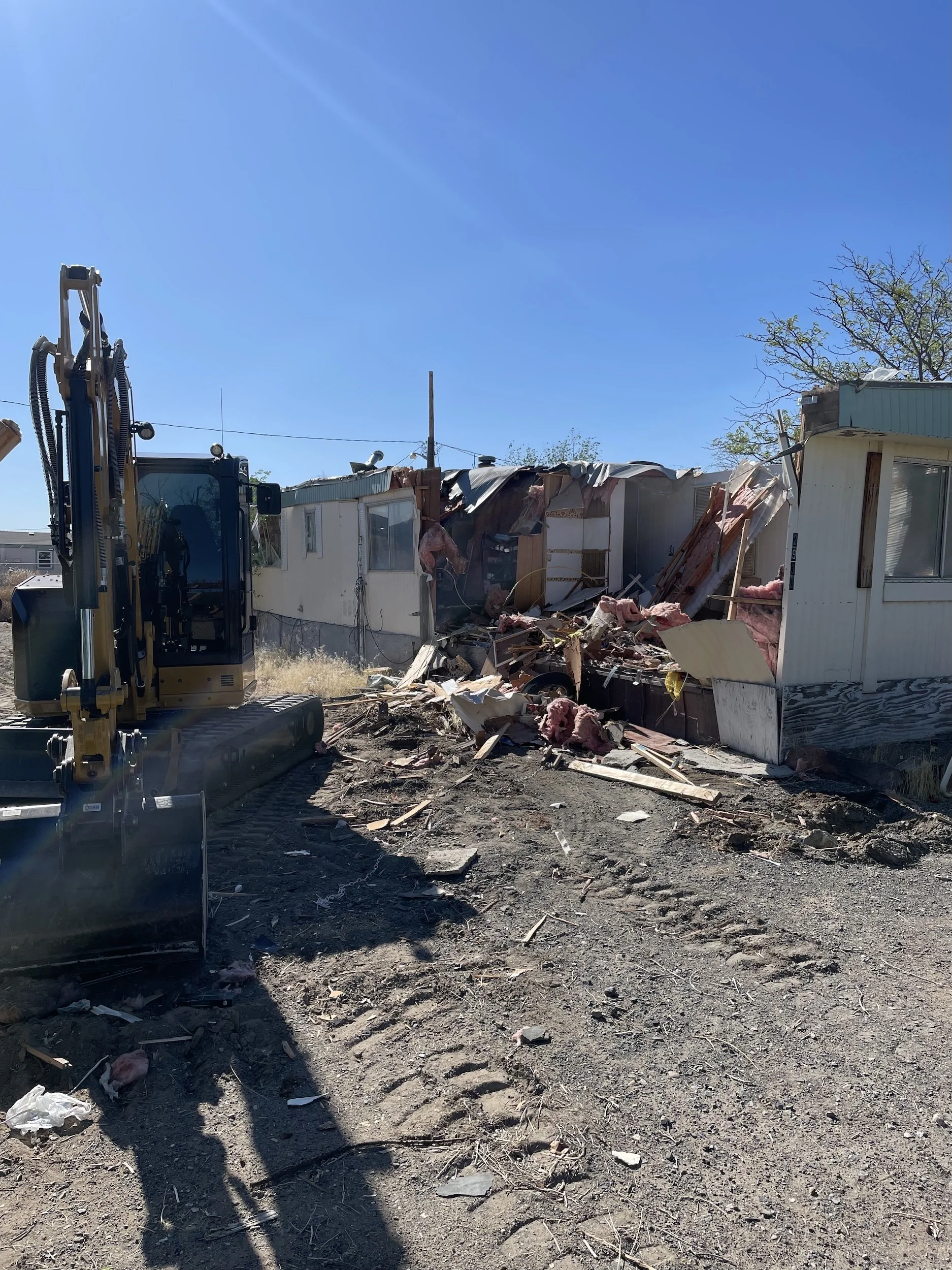 Excavator working among demolition debris beside a structure