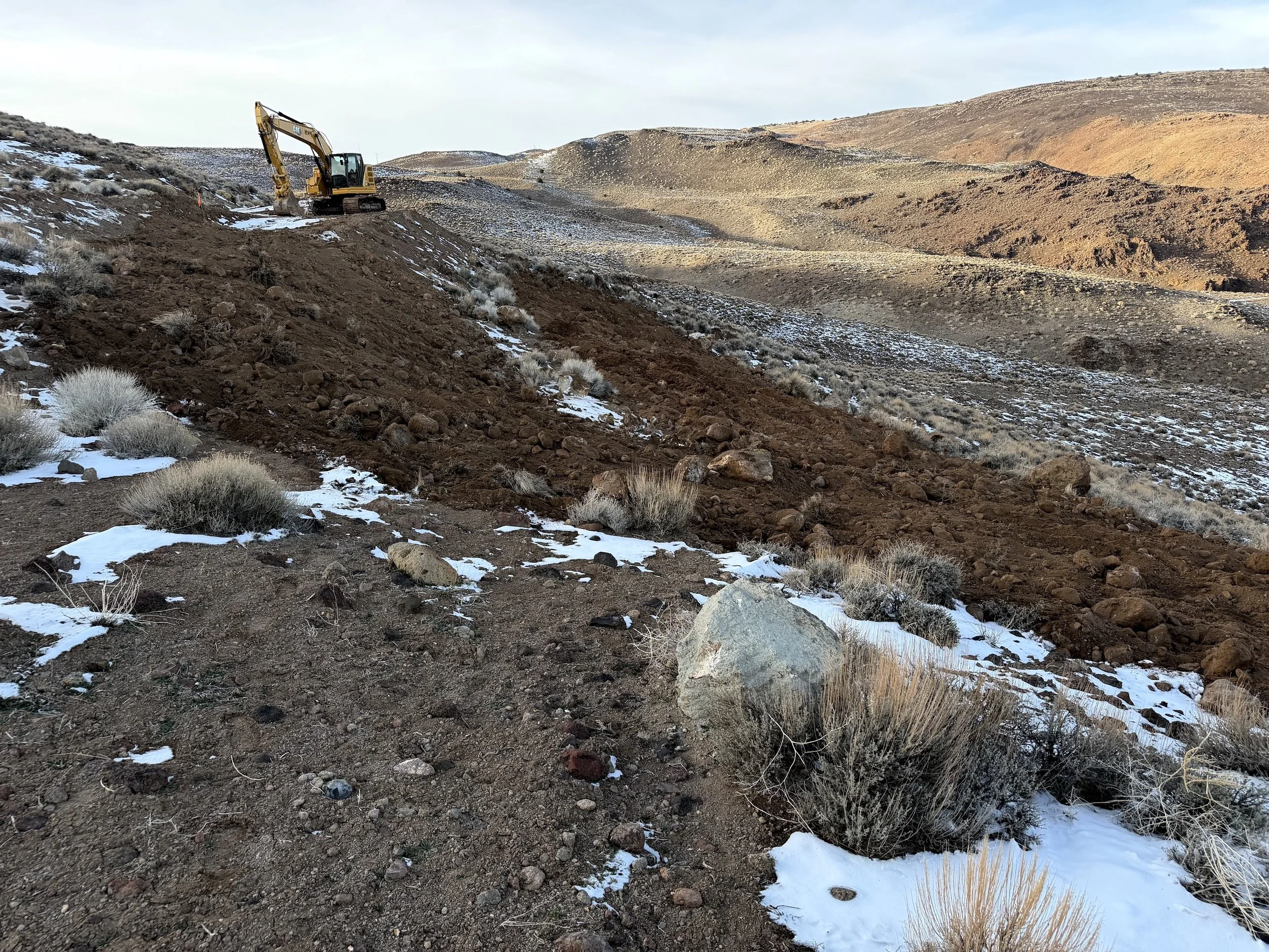 Excavator grading open space on a snowy high-desert hillside in Northern Nevada