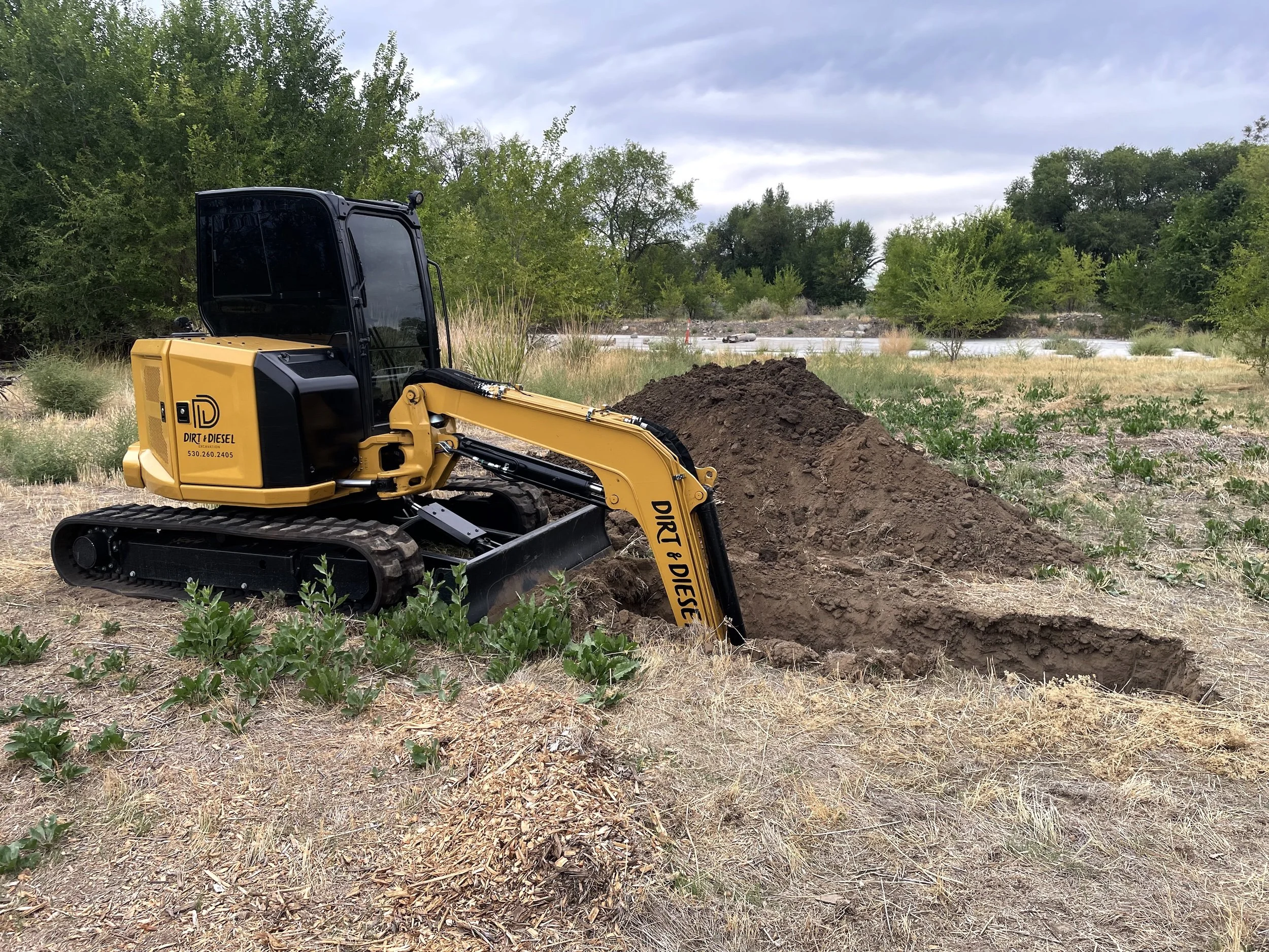Excavator digging in a grassy field during septic site preparation