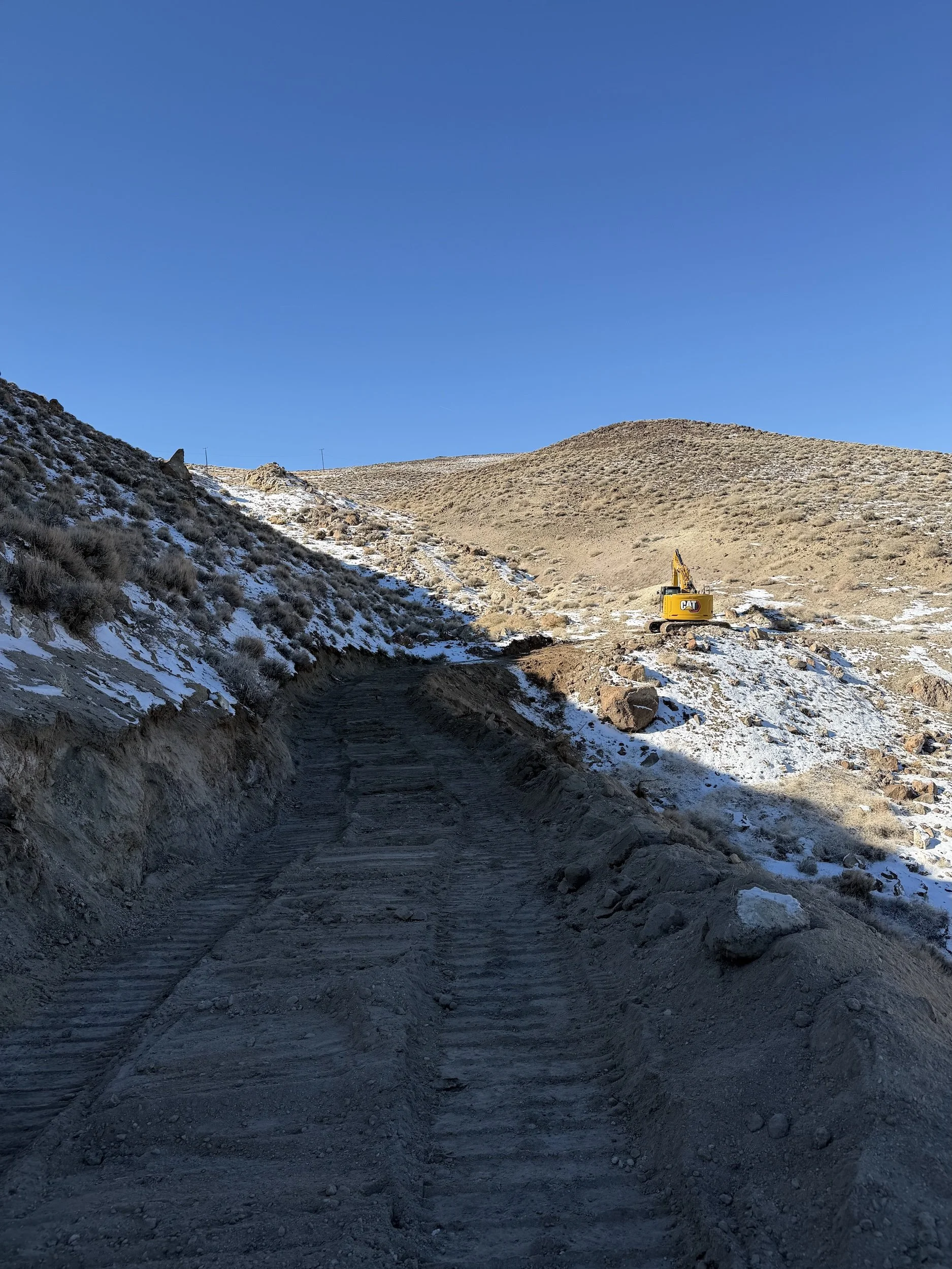Dirt road up a snowy sagebrush hillside with an excavator in Northern Nevada
