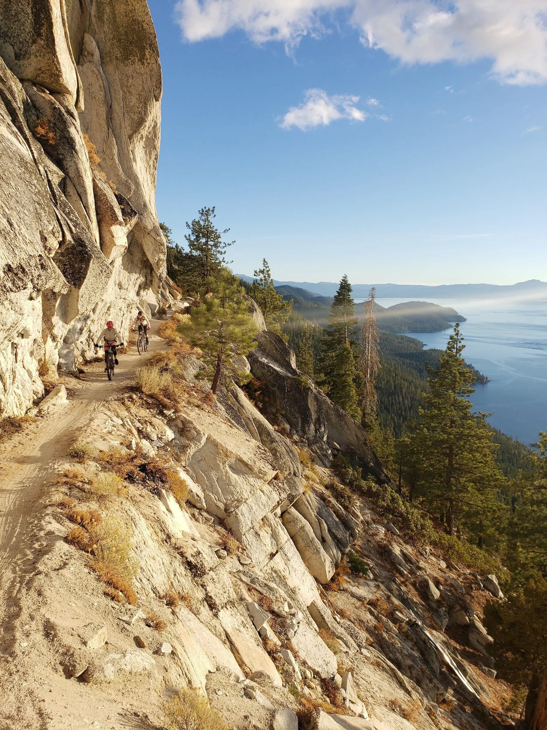Mountain bikers riding a narrow cliffside trail above Lake Tahoe