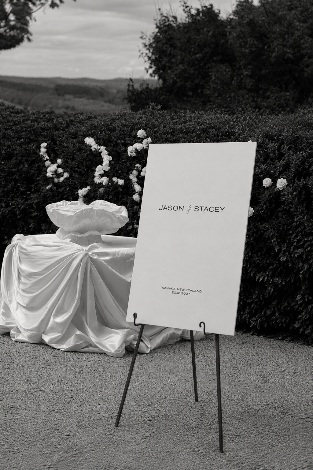 Wedding welcome sign with the names Jason and Stacey, set outdoors with a hedge and hills in the background.