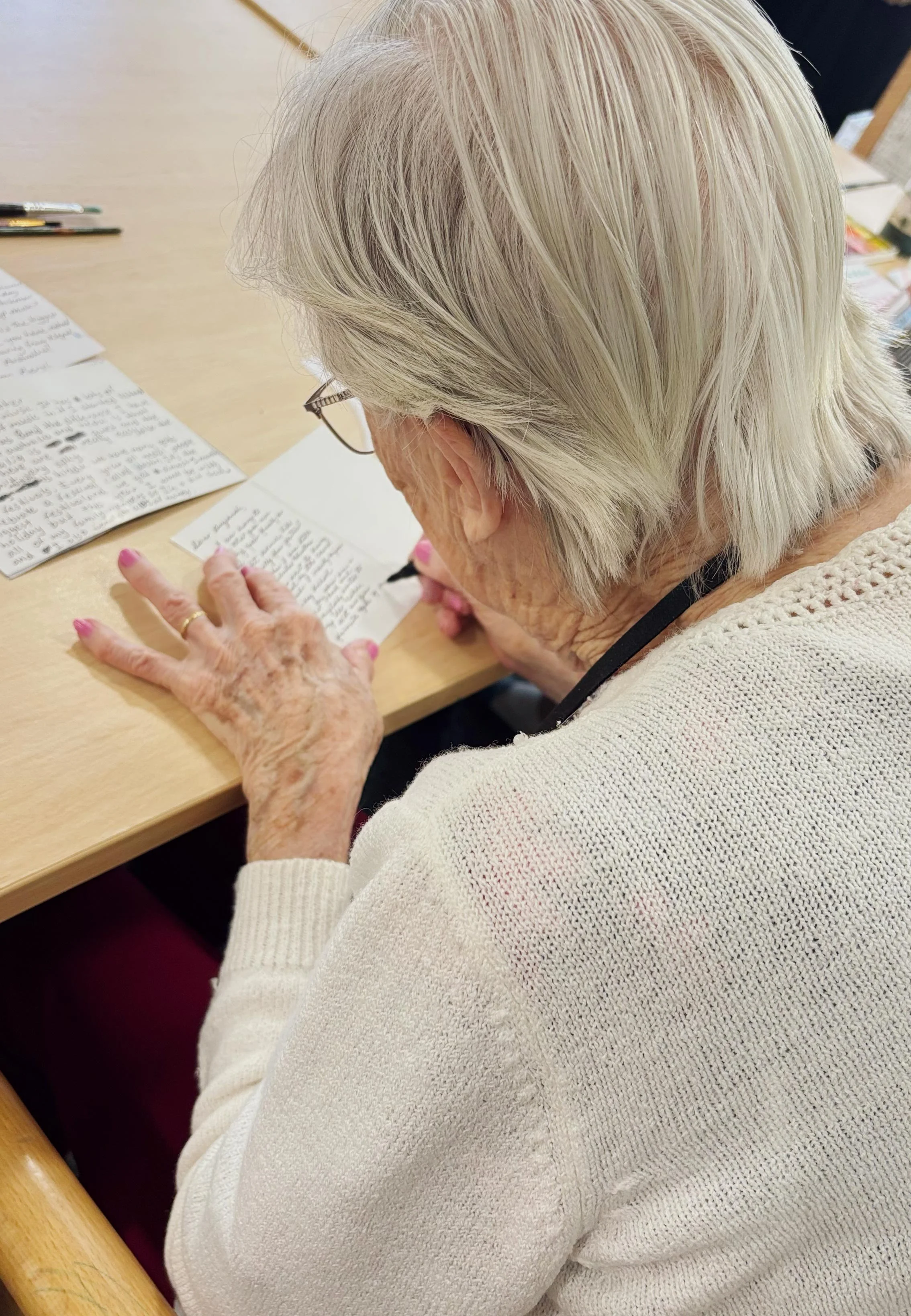 An elderly participant photographed over their shoulder as they write on the back of a postcard