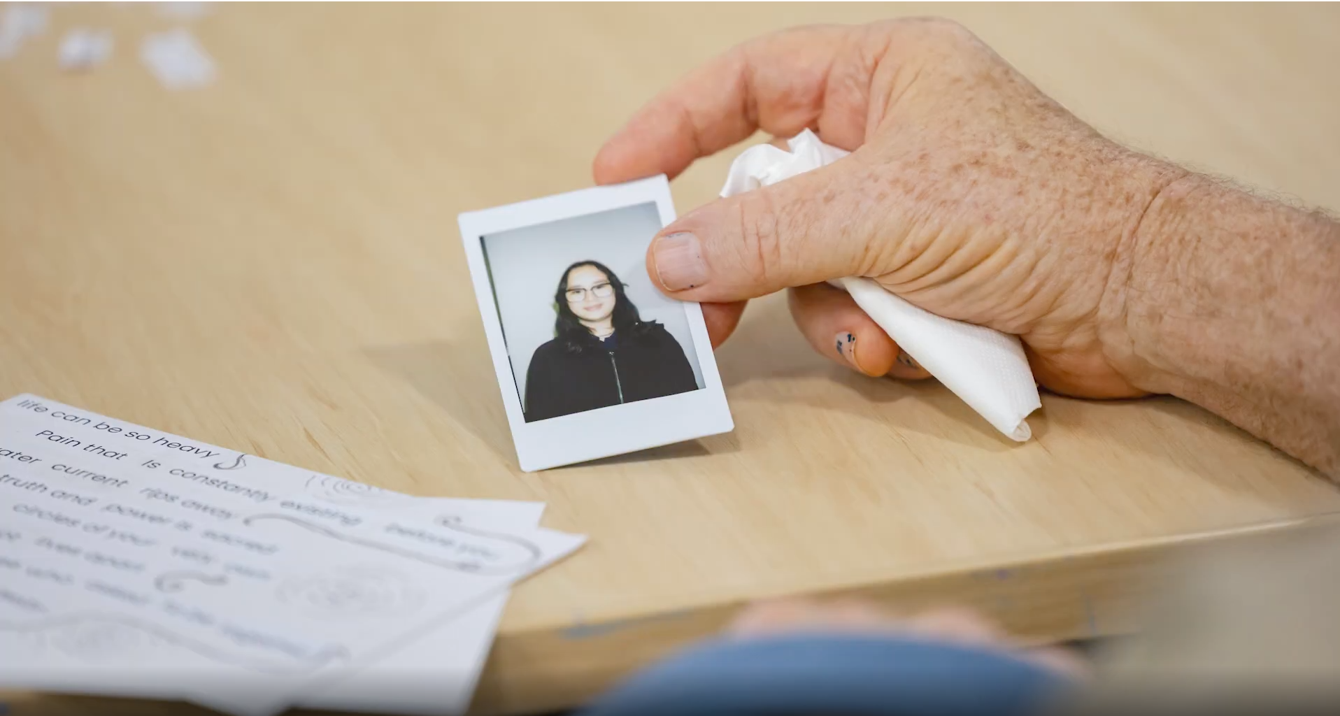 An elderly person's hand holding a polaroid photograph of a young participant