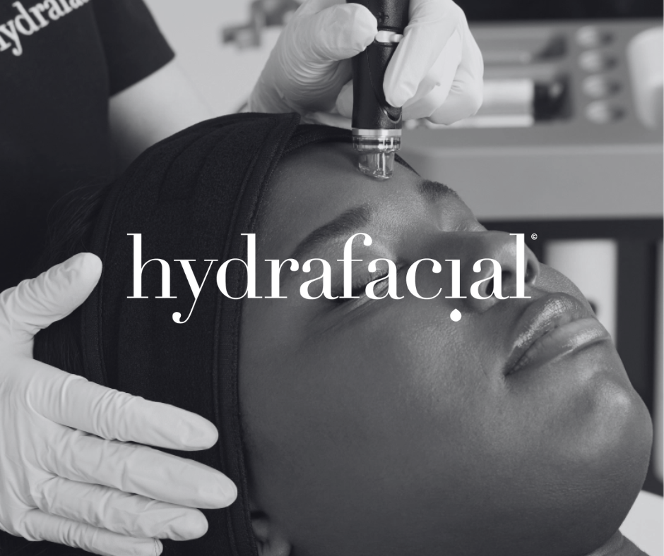 A person receiving a hydrafacial treatment with a device on their forehead, while lying down with a black headband and medical gloves, in a clinical setting.
