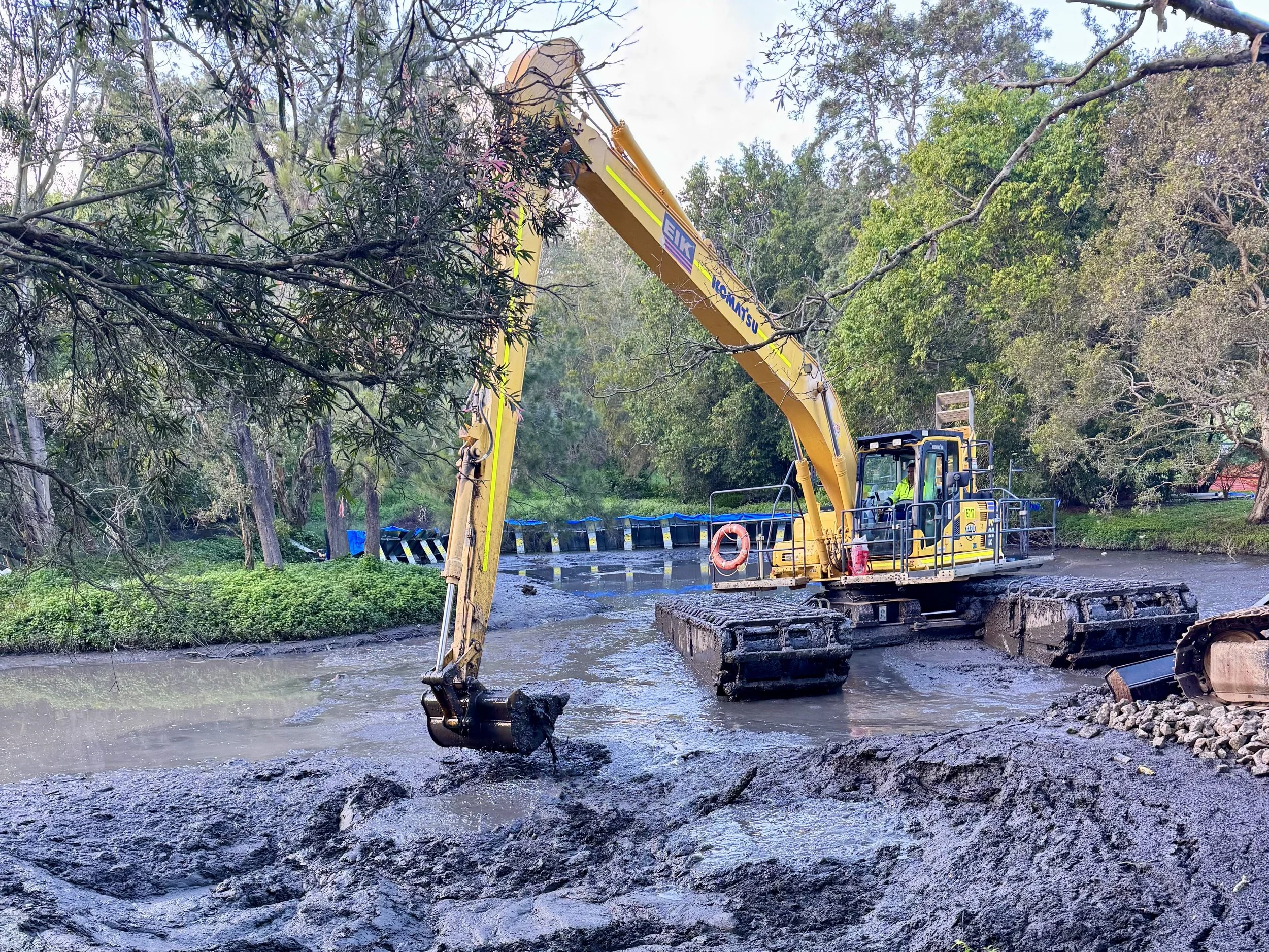 A construction excavator working in a river, cutting or removing a fallen tree or branch.