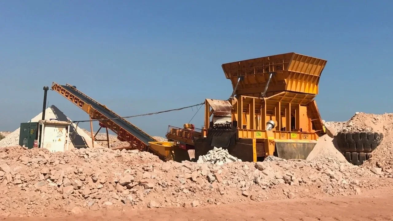 A large industrial rock crusher machine operating in a quarry to break rocks into smaller pieces with a conveyor belt transporting rocks away.