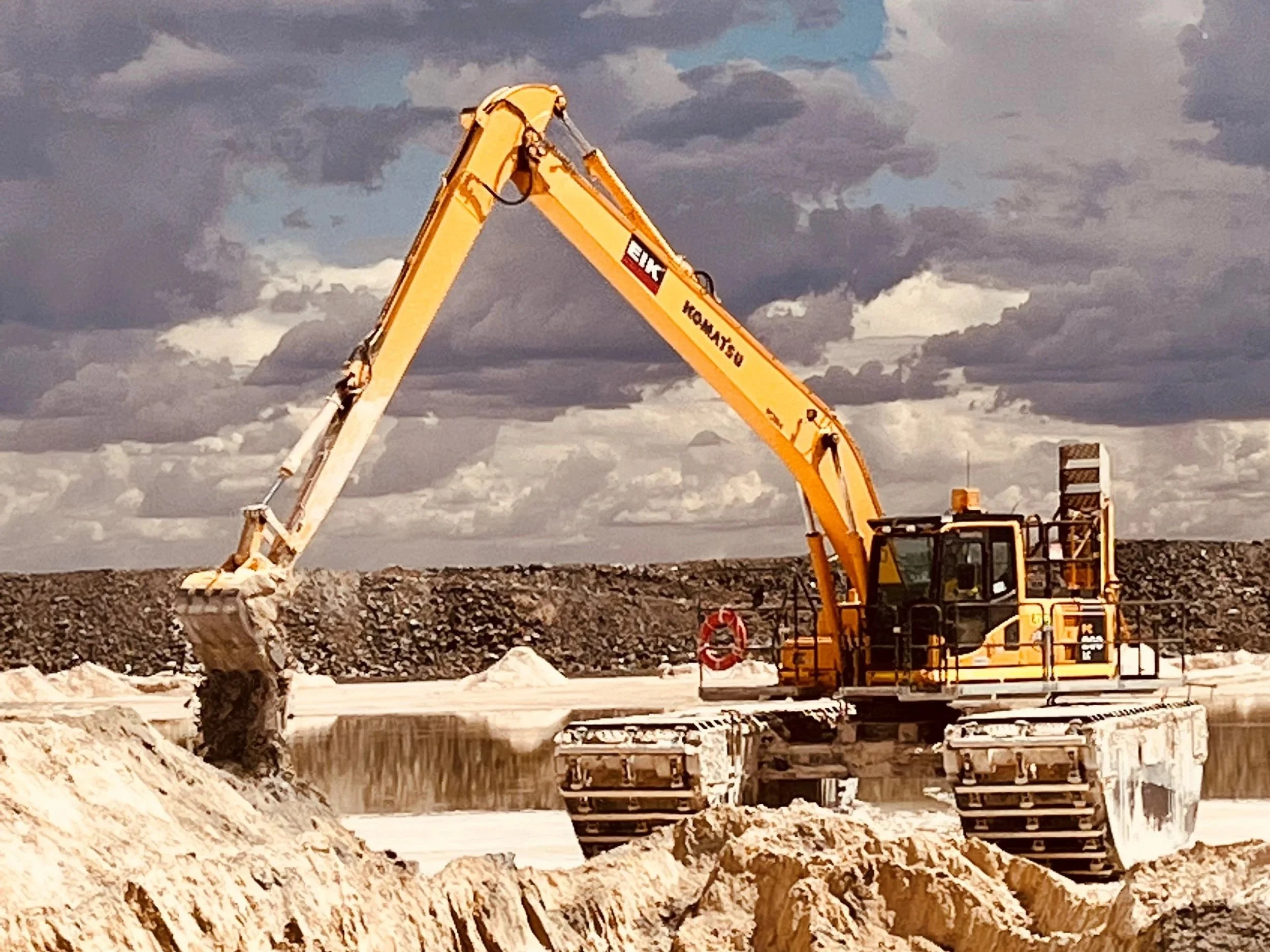 A construction excavator working on a construction site under a cloudy sky.