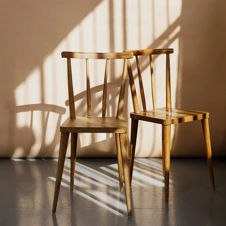 Two wooden chairs casting shadows on a beige wall, illuminated by sunlight.
