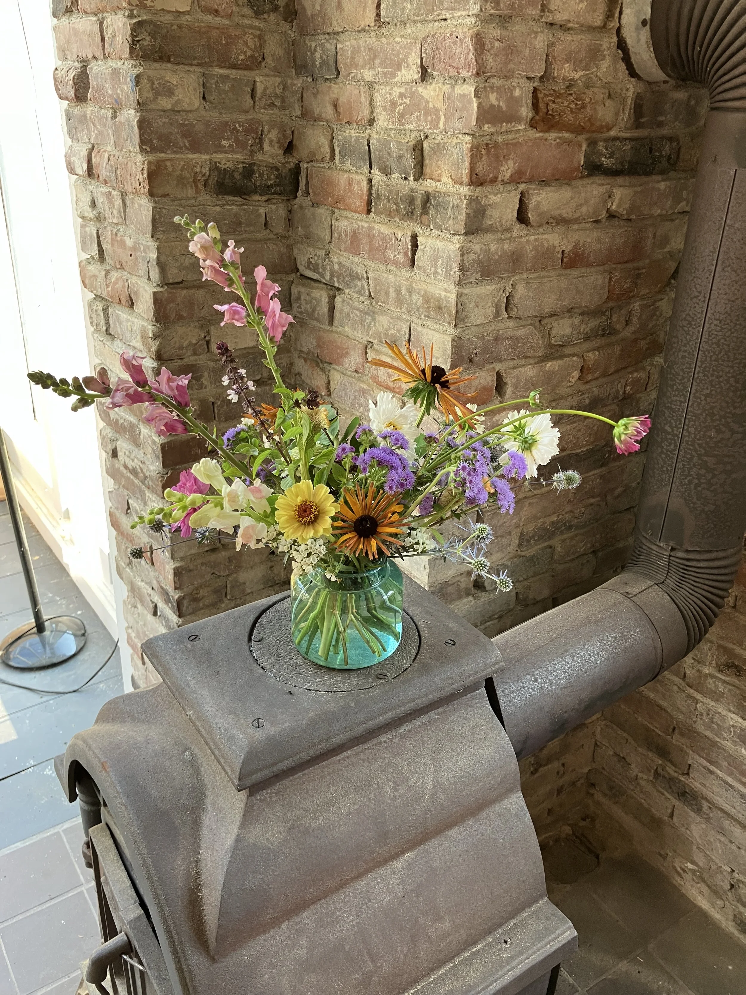 The floral centerpiece contains snapdragons, rudbeckia, cosmos, and zinnias. It has a relaxed, beach party design style. 