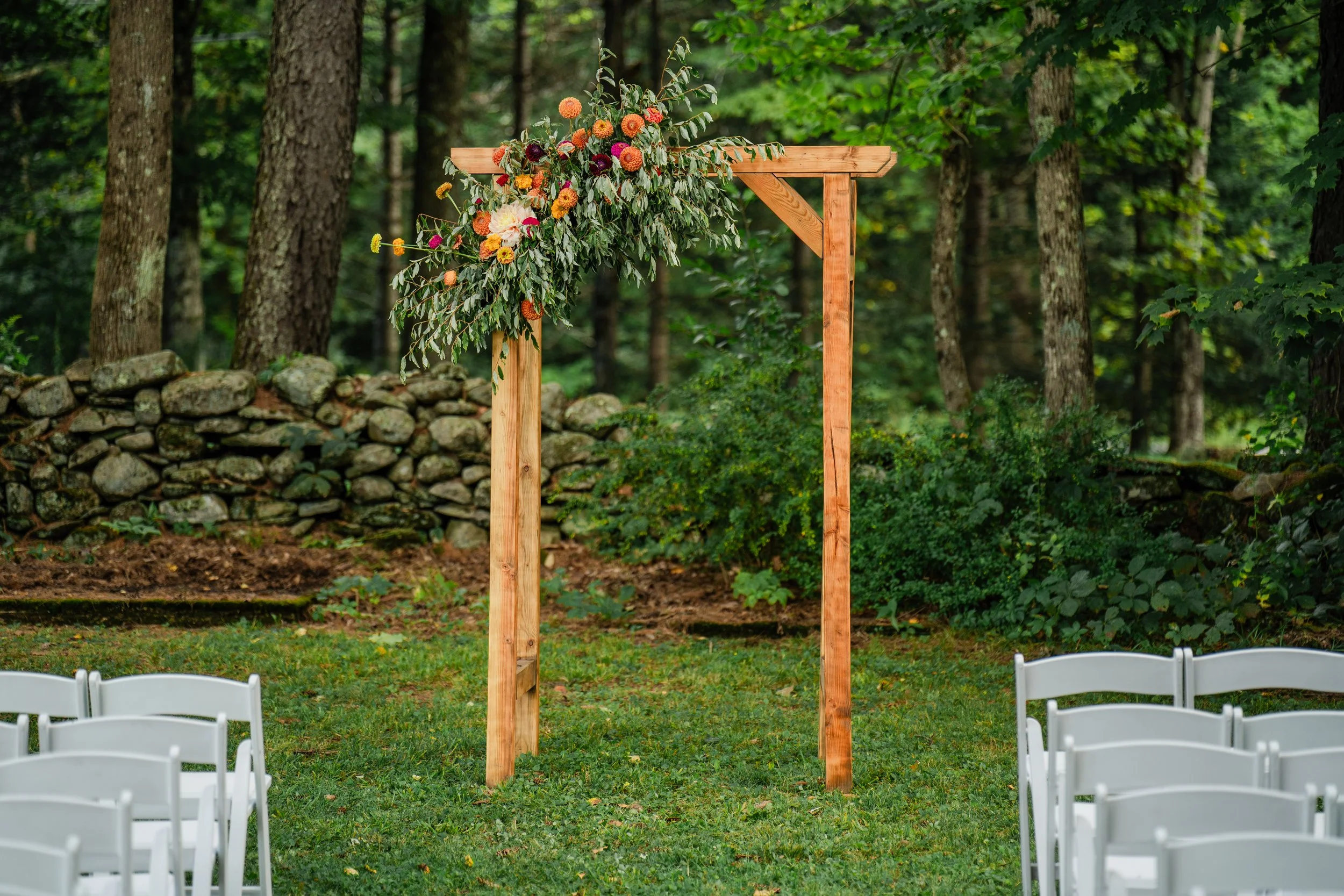 A rustic wooden arch stands at a garden party themed wedding. The arch is adorned with local fresh flowers. 