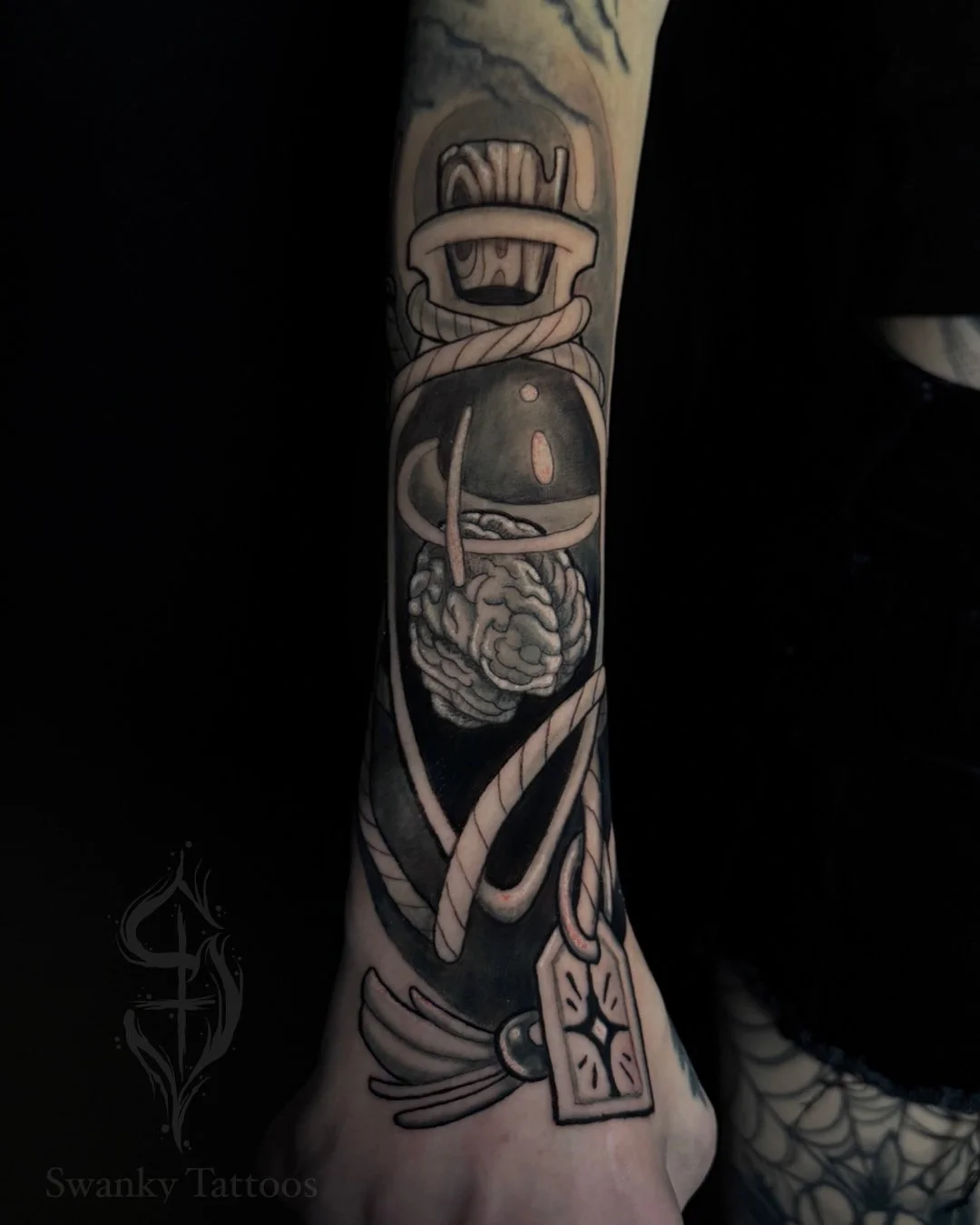 Black and gray tattoo on a person's arm featuring a stylized cartoon bomber plane with a rope wrapped around it, a brain, and a dagger near the wrist.