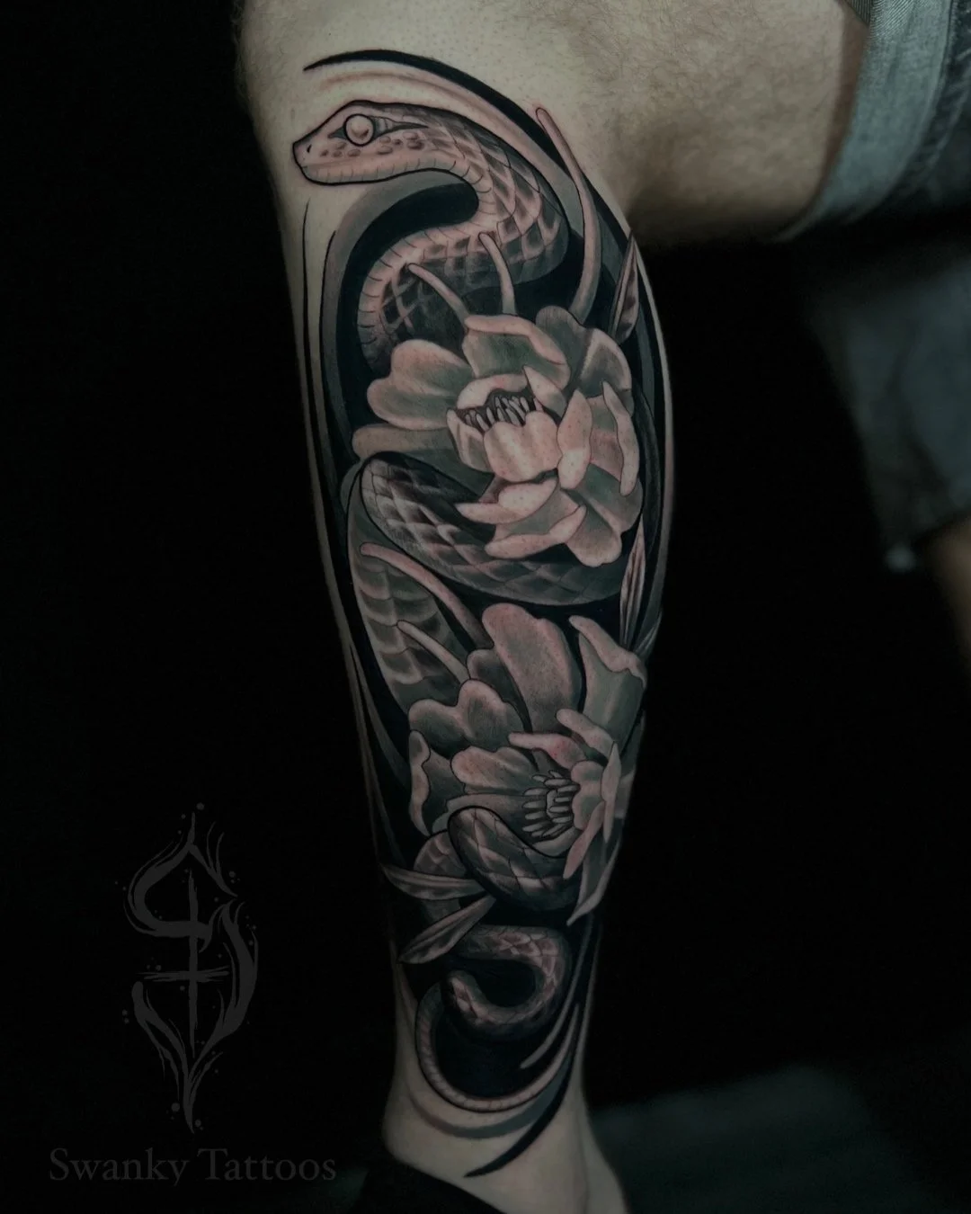 Black and gray tattoo of a snake intertwined with flowers on a person's arm.