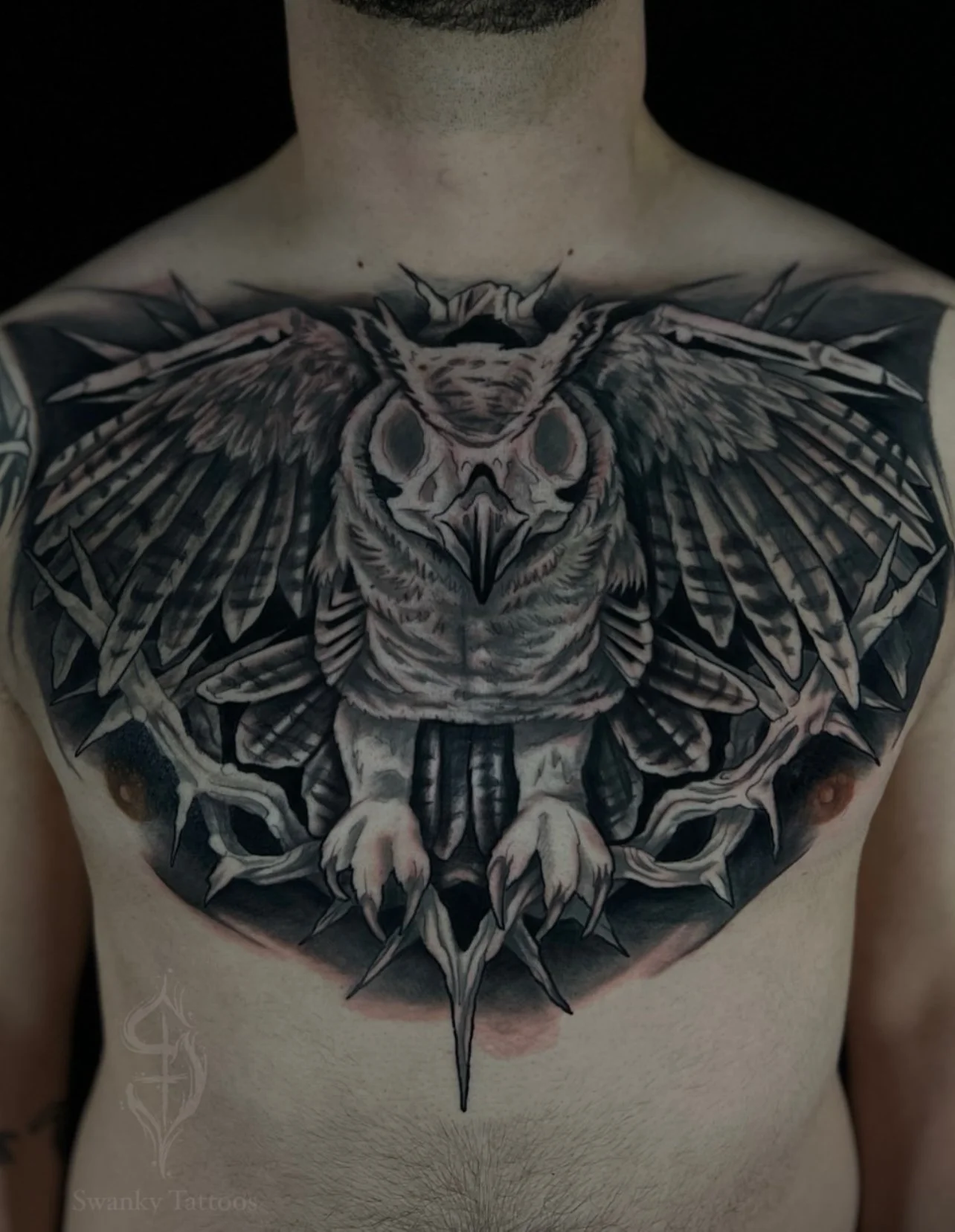 Black and gray tattoo of an owl with outstretched wings on a person's chest, surrounded by thorny branches.