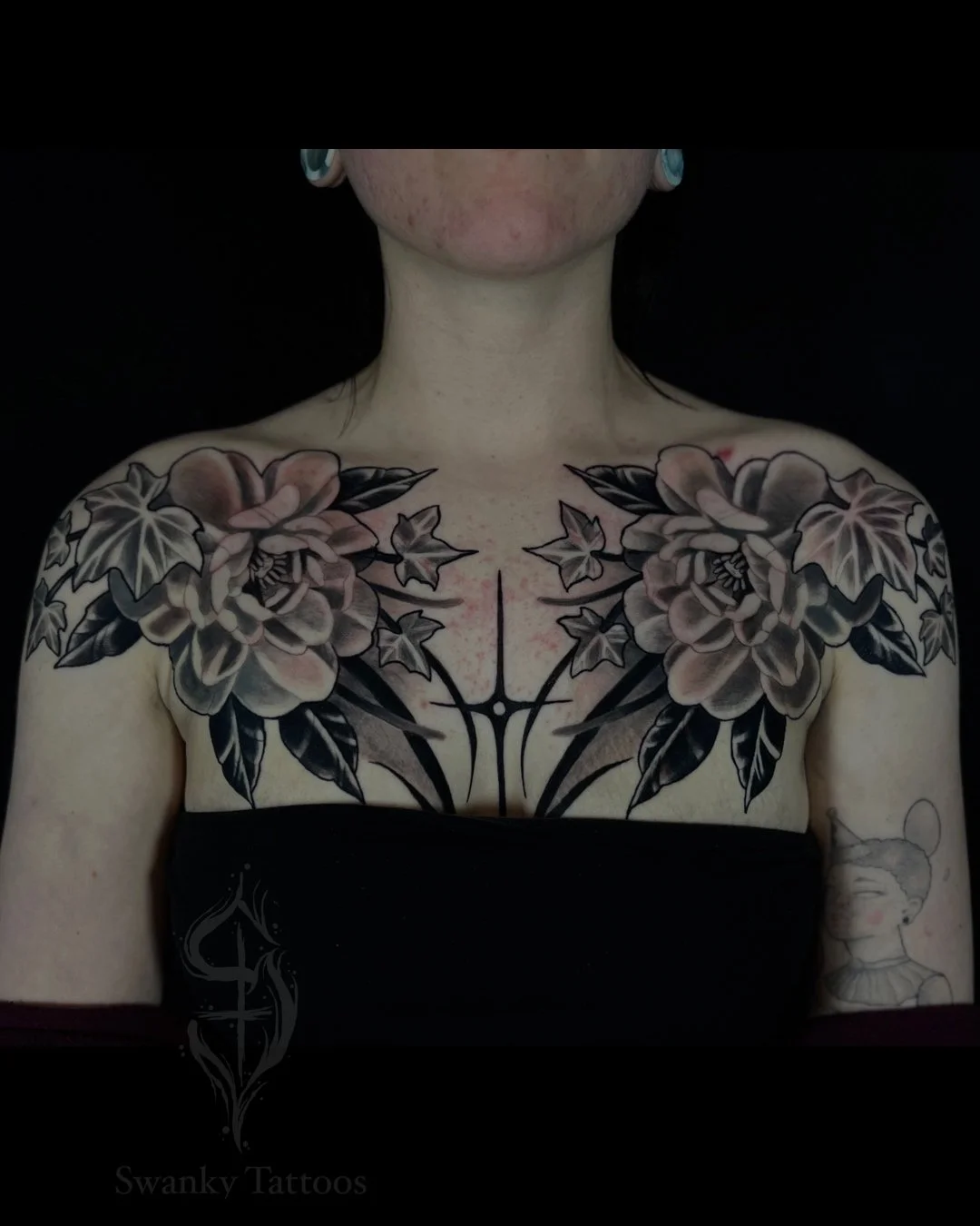 Black and gray floral chest tattoo with large flowers and leaves across the shoulders and upper chest.