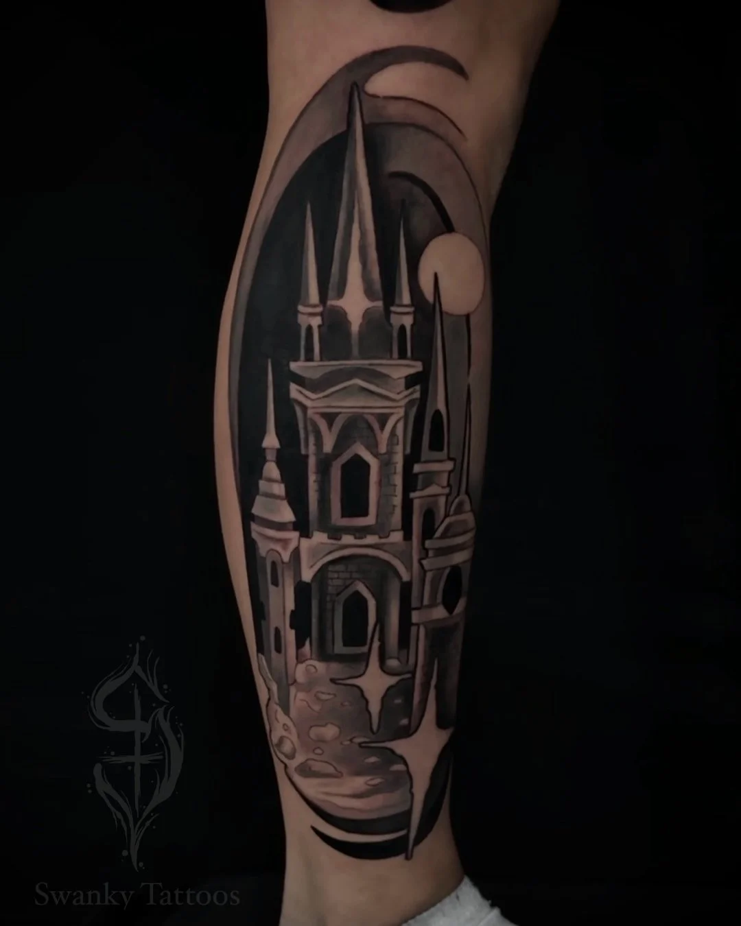 Black and gray tattoo of a castle with tall spires, set against a night sky with a moon, on a person's arm.