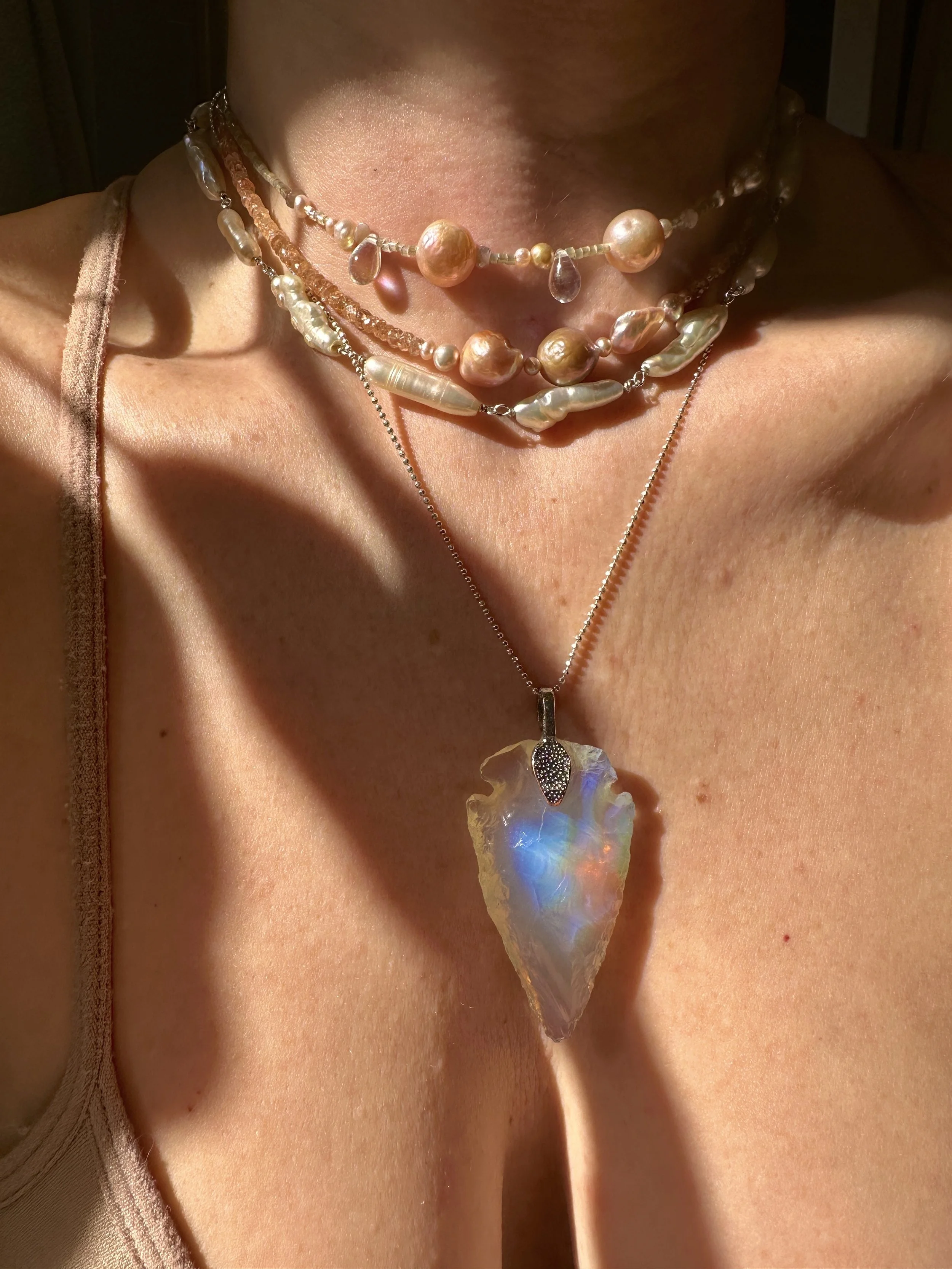 stack of pearl chokers with arrowhead opal glass pendant.