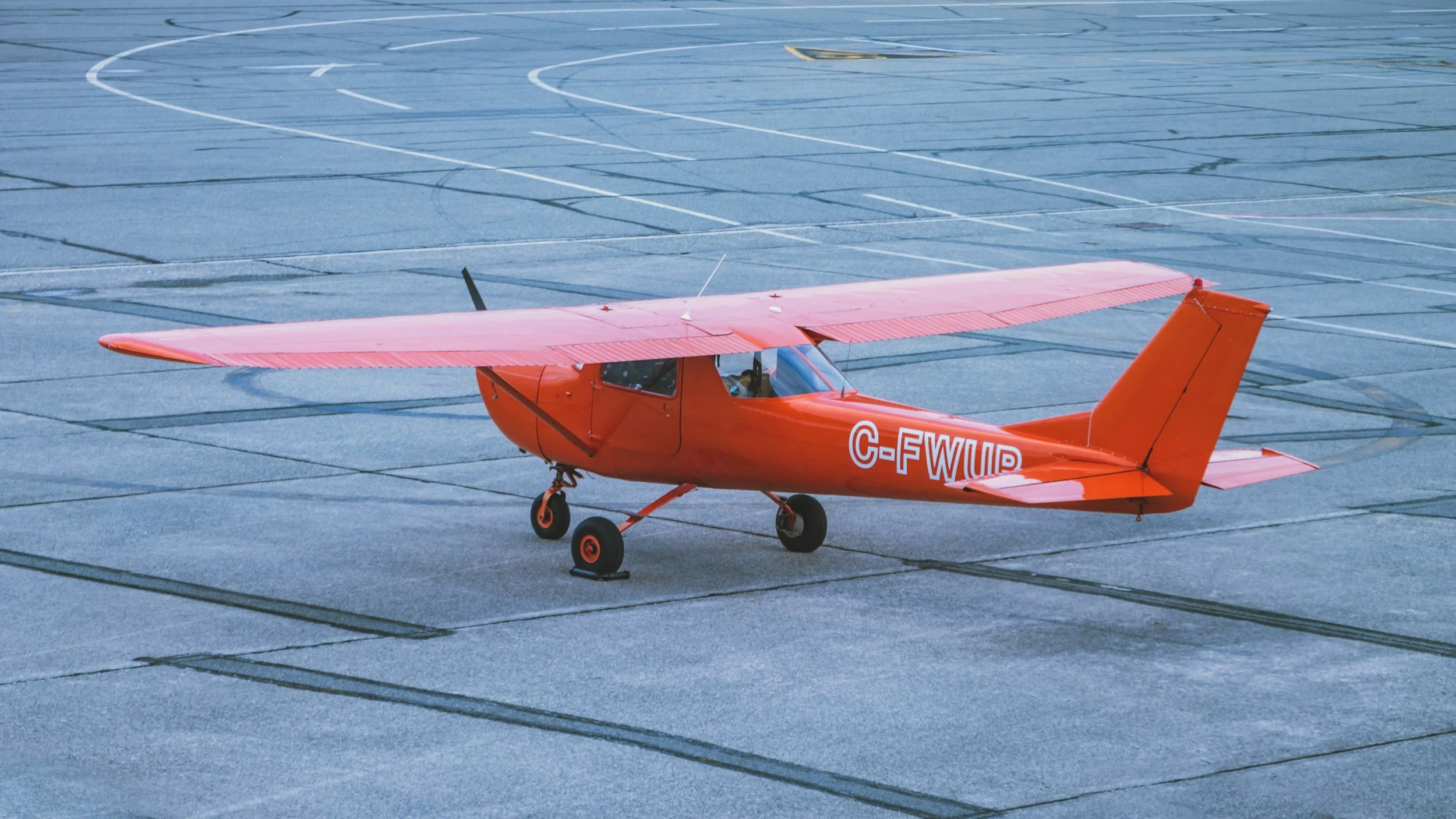 Small red single-engine airplane parked on an empty tarmac with painted lines.