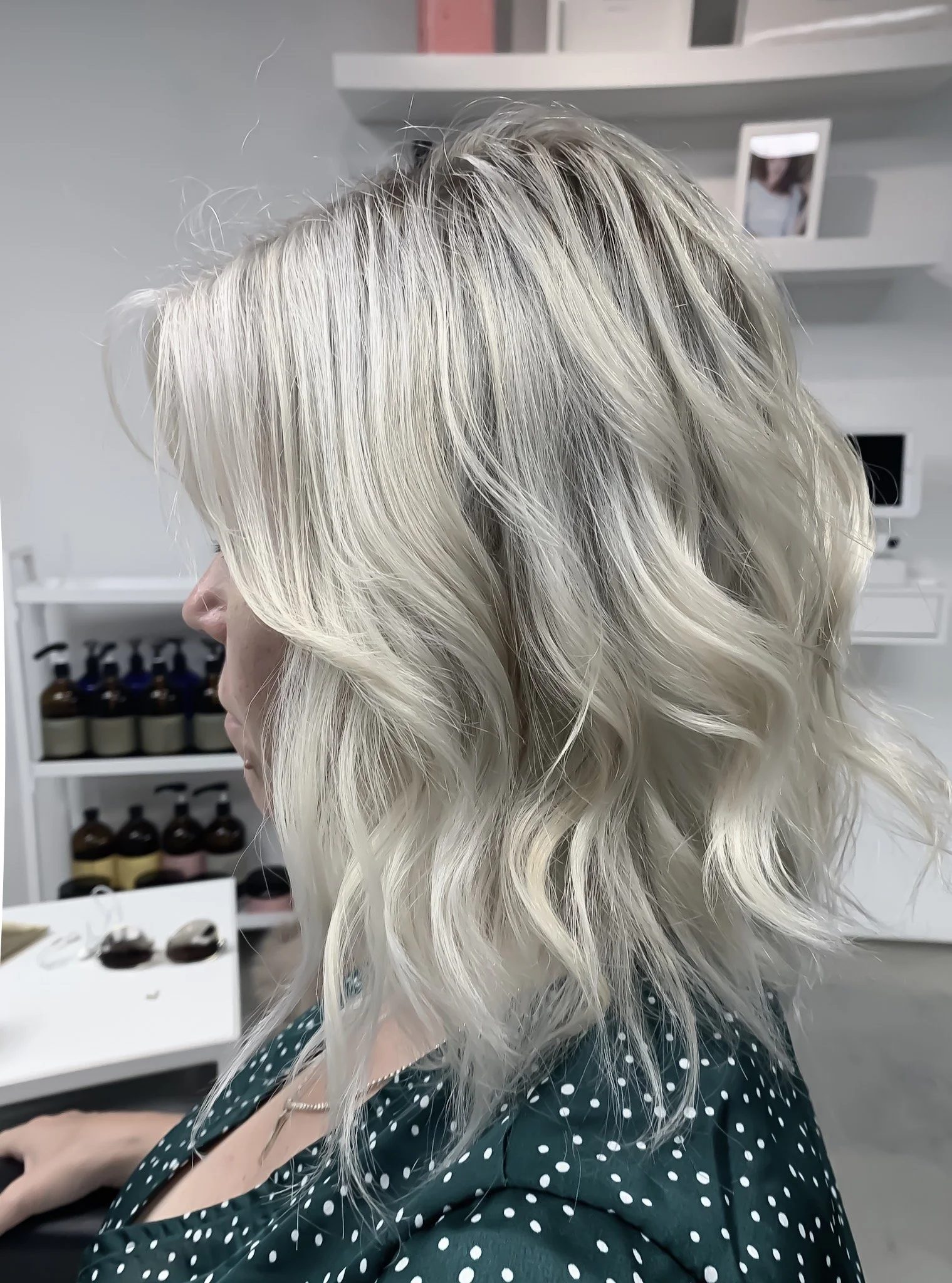 Woman with blonde, wavy hair and a green polka dot top in a salon.