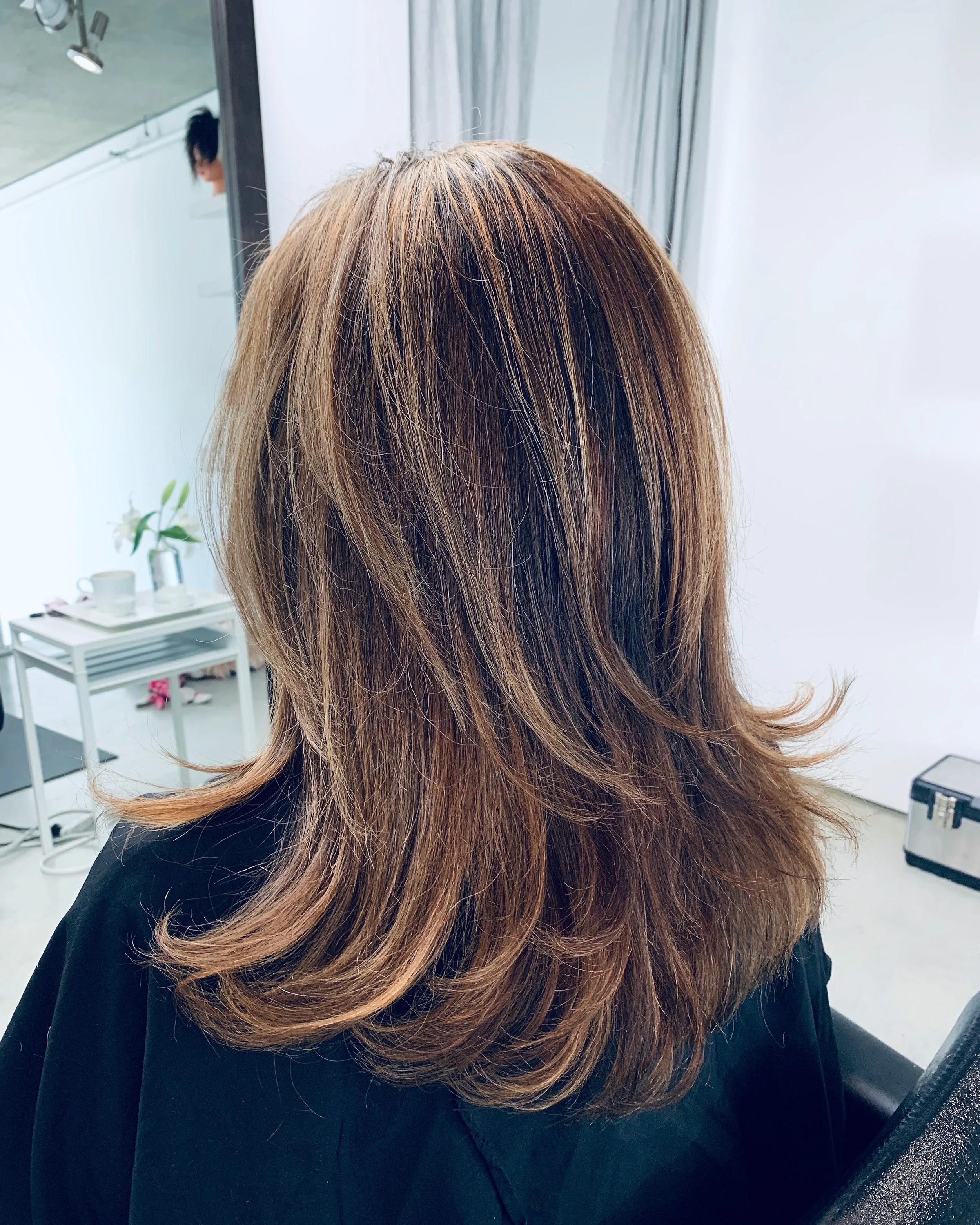 Woman with layered brown hair in a salon, sitting in front of a mirror.
