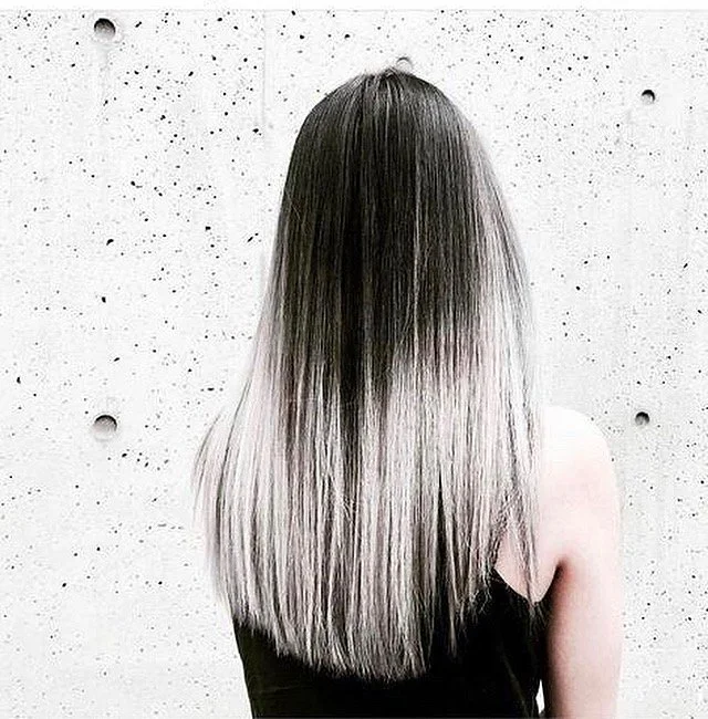 Back view of person with long, straight, ombre hair in black and white, against a textured concrete wall.