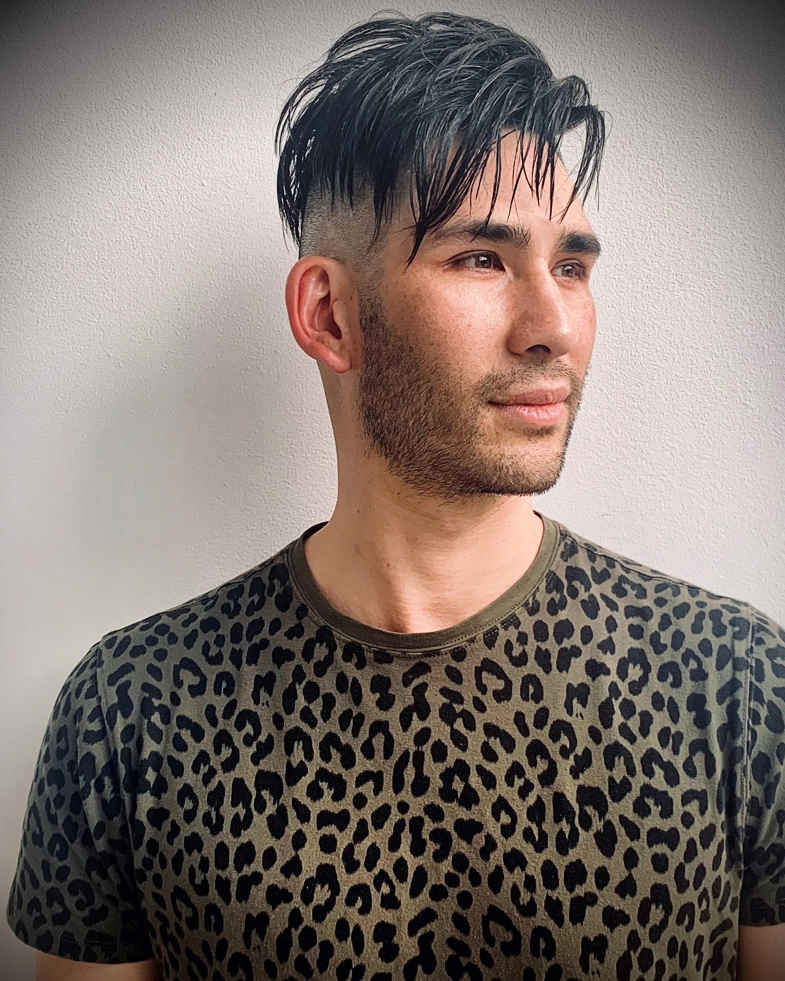 Man with dark hair and undercut wearing leopard print shirt.