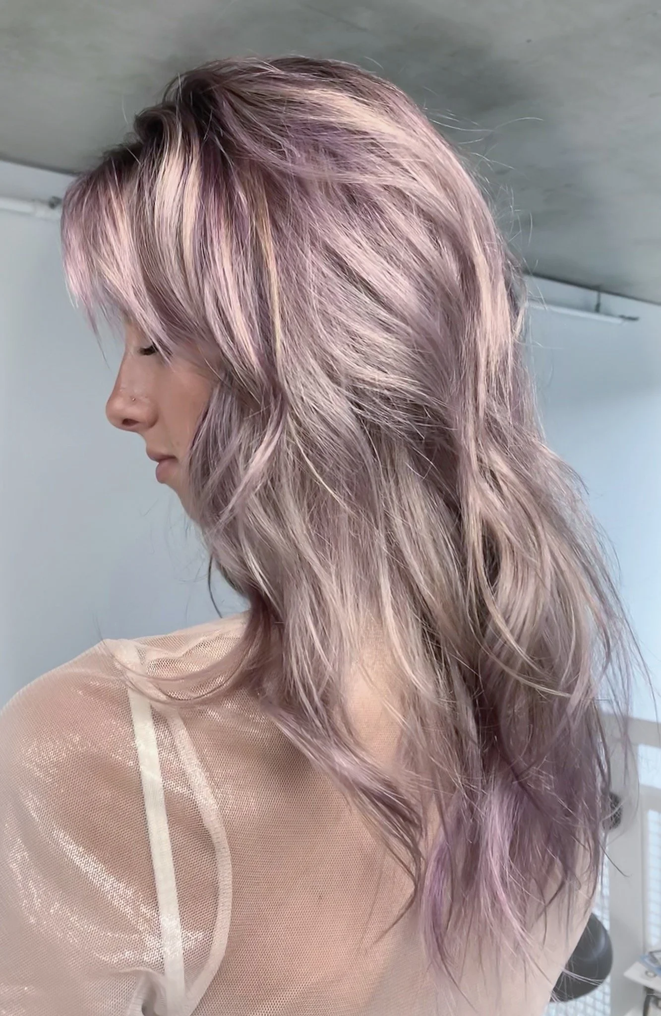 Woman with long, wavy, pastel purple hair and sheer top, side profile