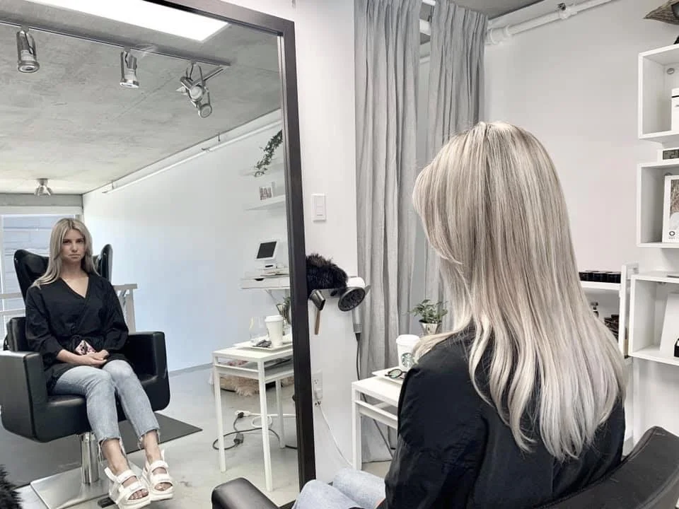 Woman with blonde hair in a salon chair facing a mirror