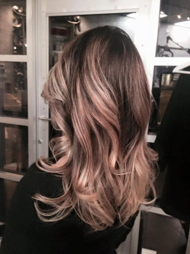 A woman's shoulder-length hair styled in soft, loose curls with a balayage color transition from dark brown at the roots to light pink at the ends.