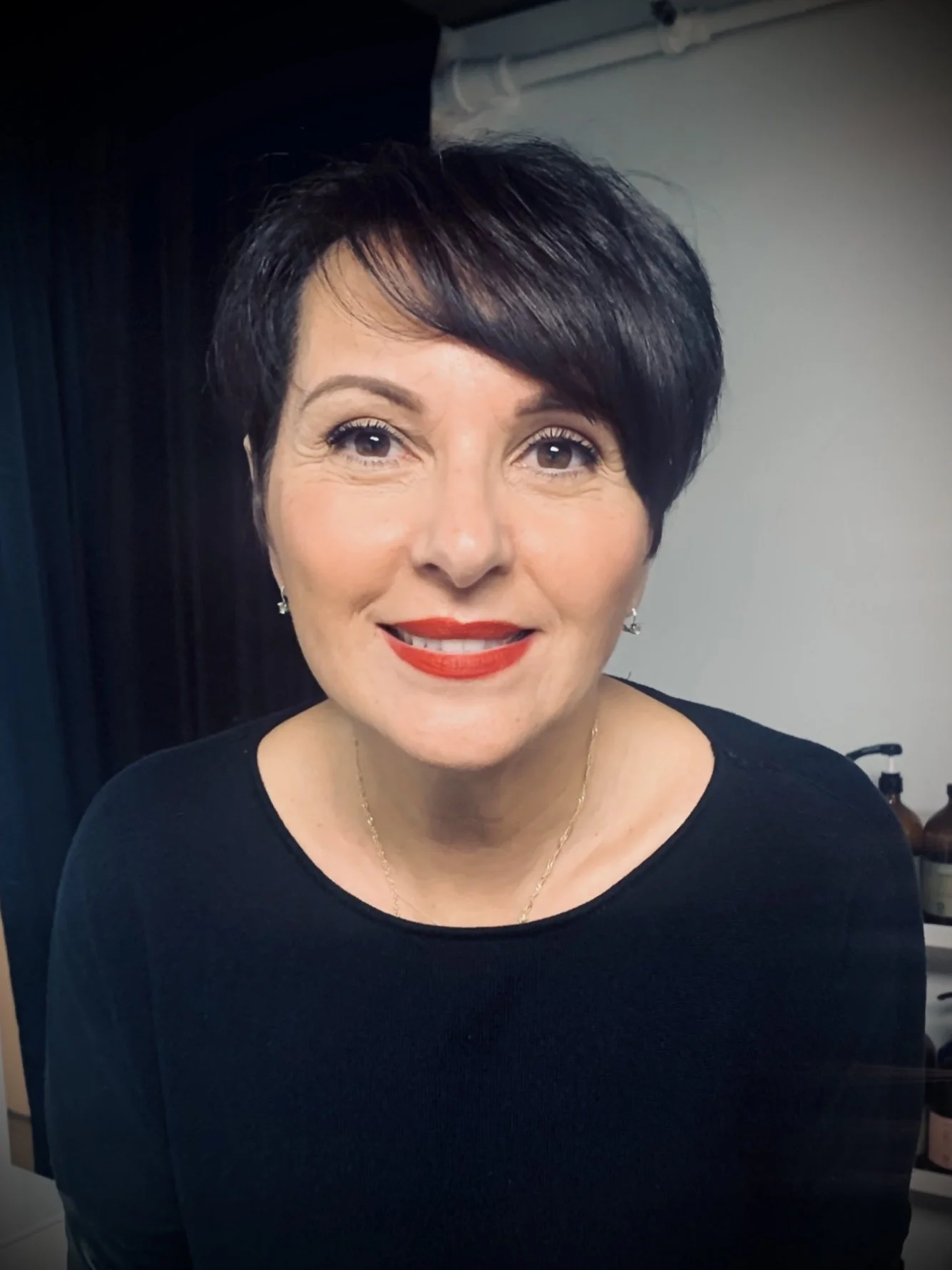 Woman with short dark hair and red lipstick smiling in a dark-colored top.