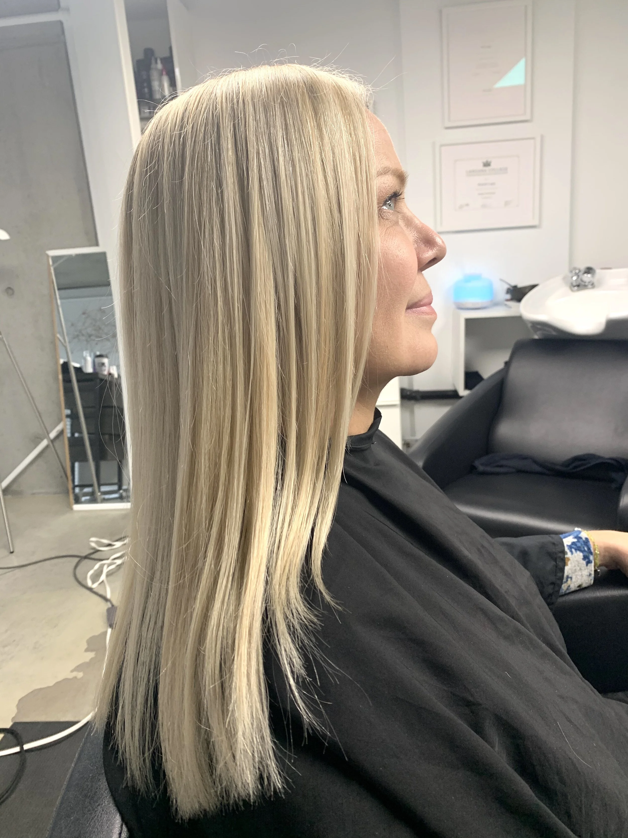 Side profile of a woman with long, straight, blonde hair sitting in a salon chair.