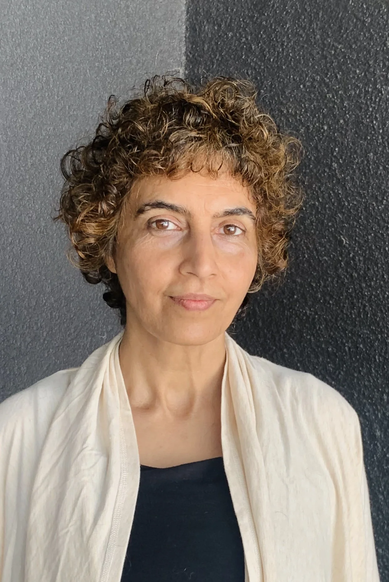 Portrait of a person with curly hair in a light-colored shirt against a dark background.