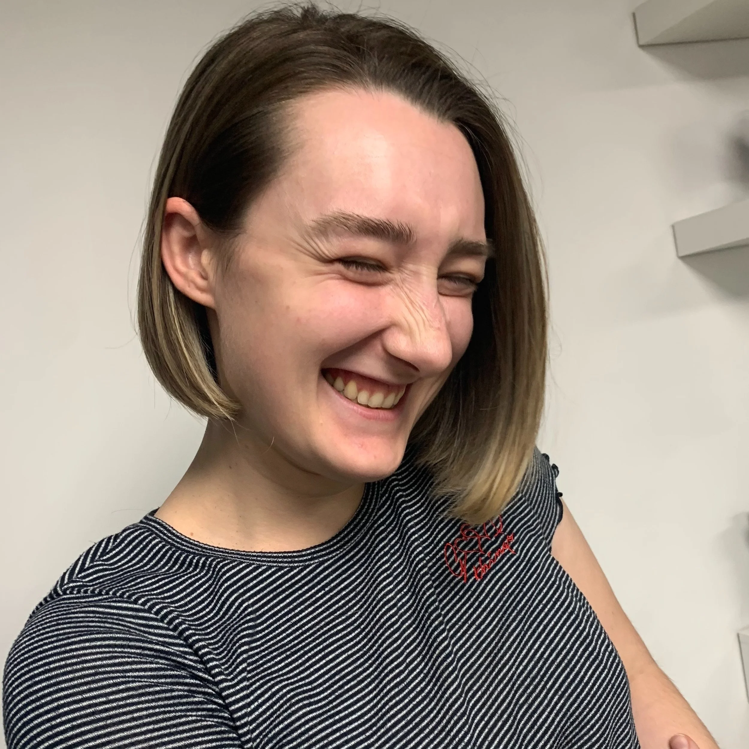 A woman with short brown hair smiling with eyes closed, wearing a striped black and white shirt.