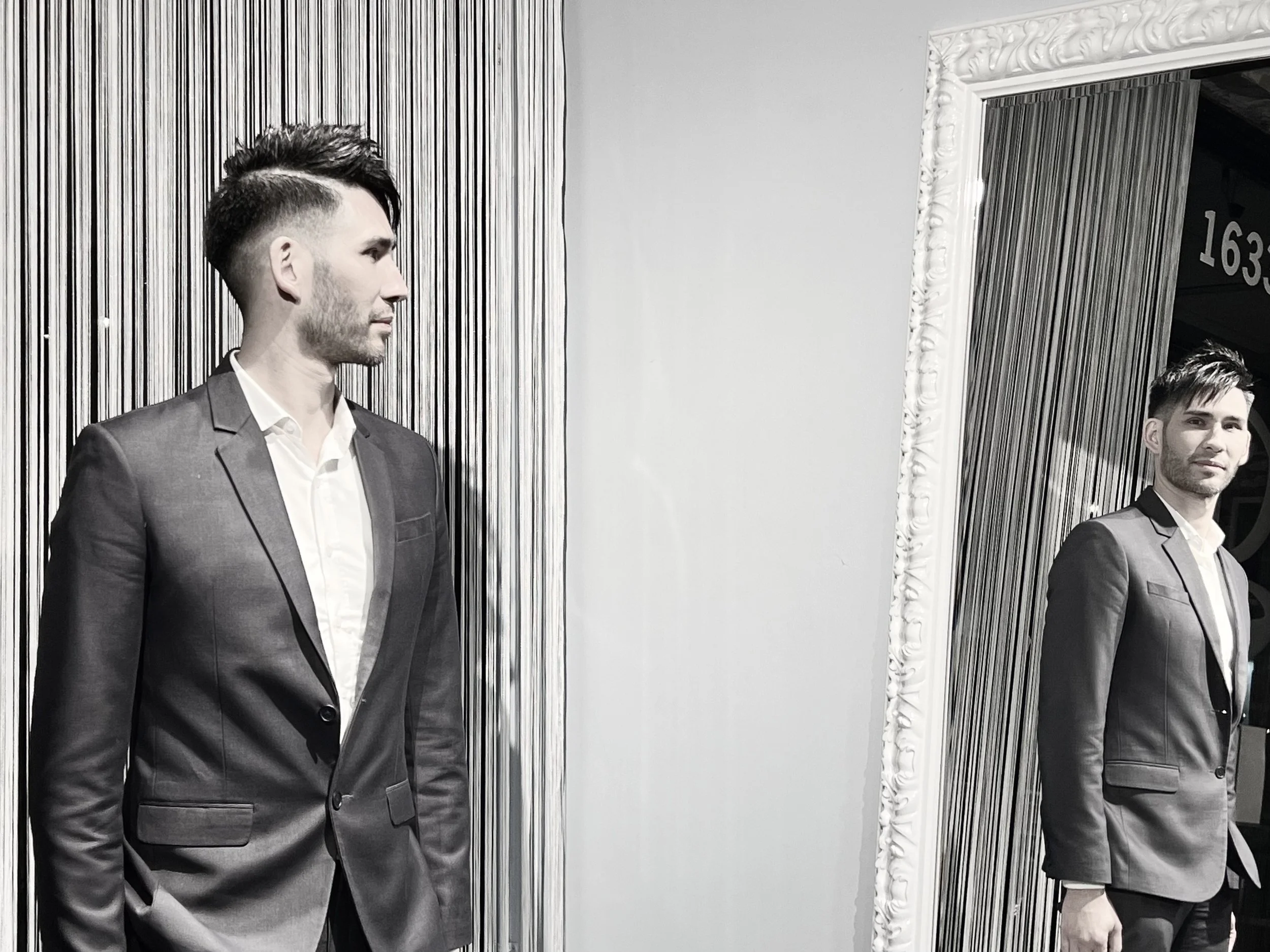 Man in a suit looking at his reflection in a mirror, monochrome setting.