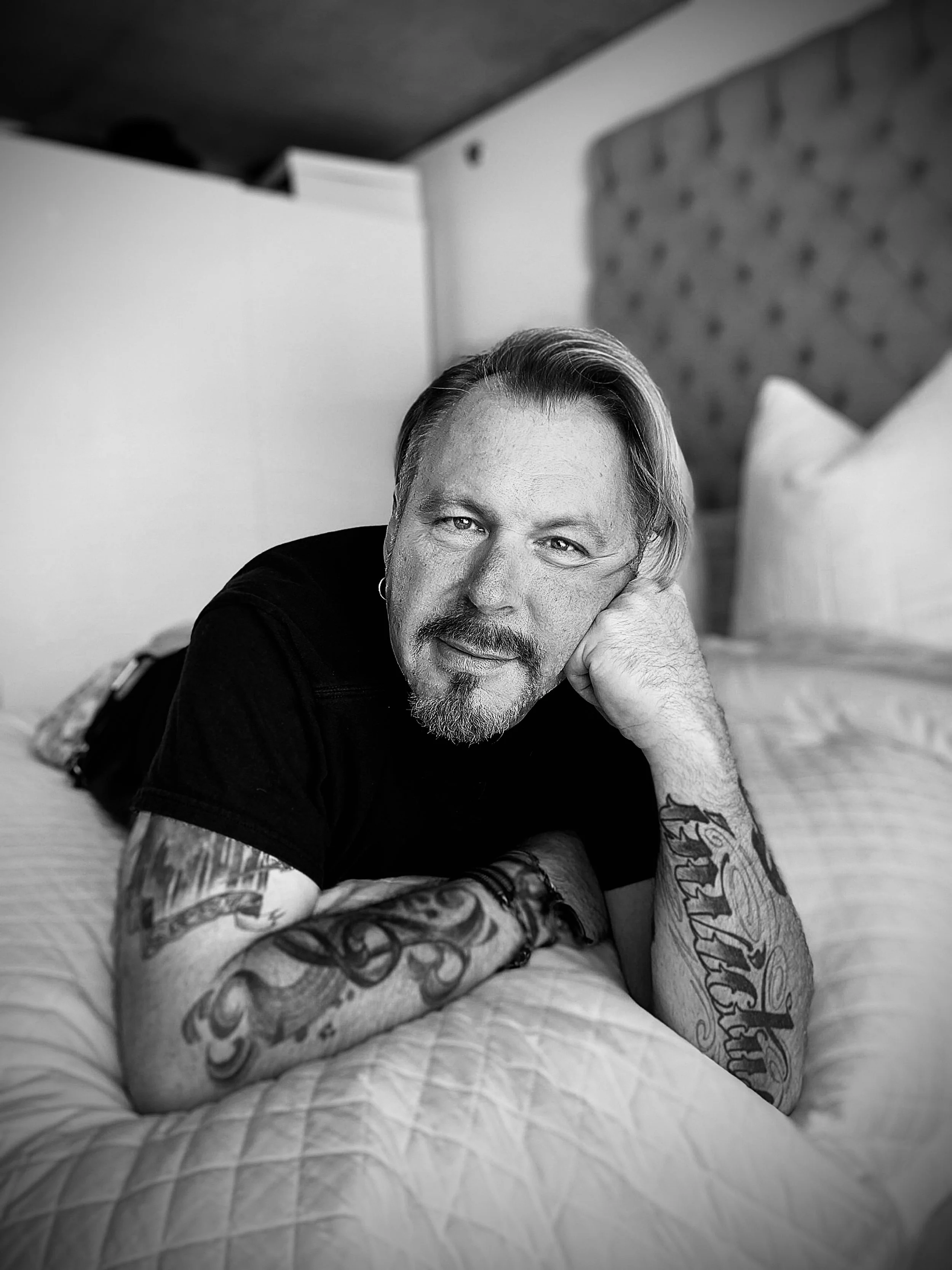 A man with tattoos lying on a bed, black and white photo.