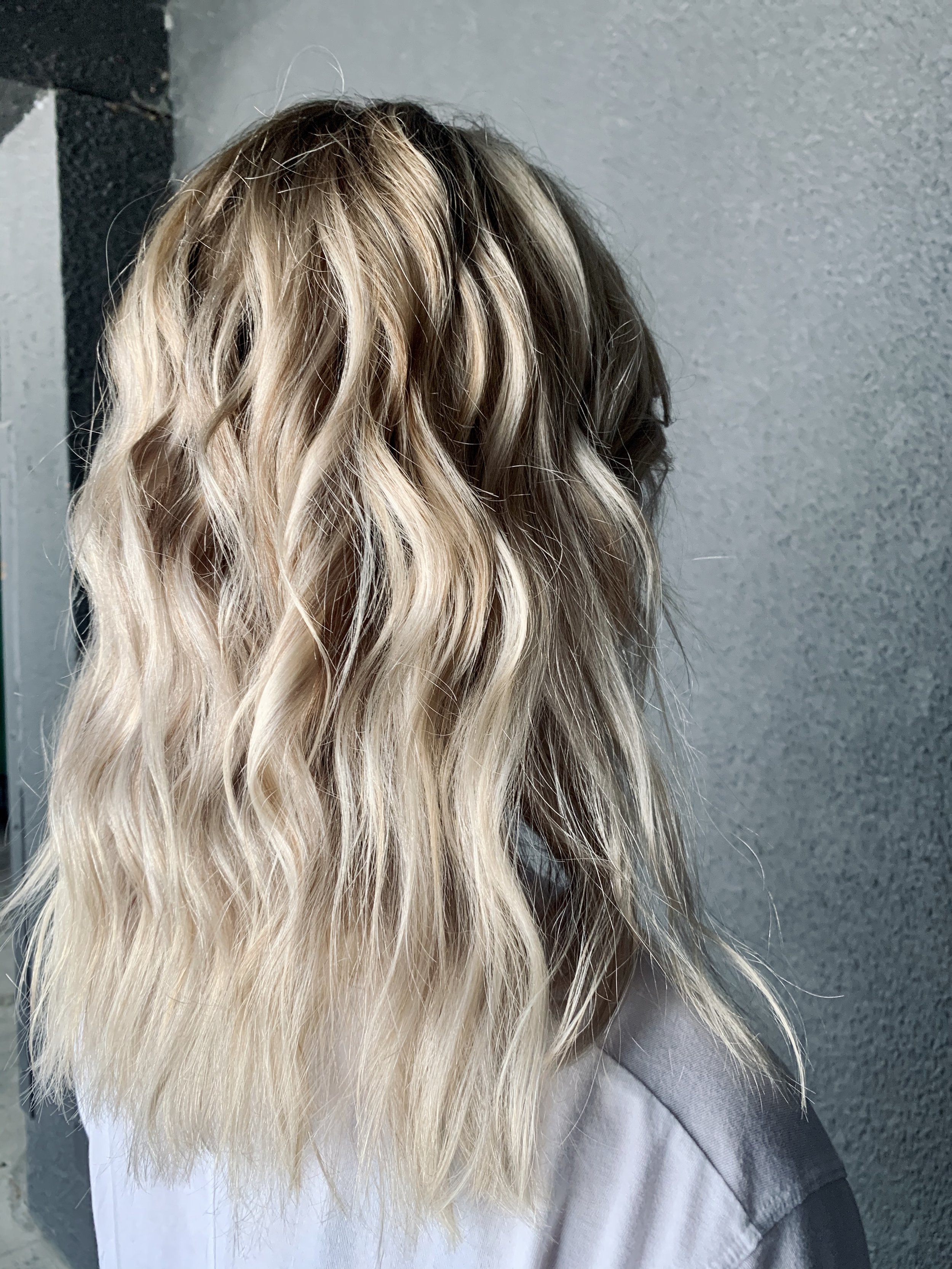 Person with wavy blonde hair and a gray shirt seen from behind.