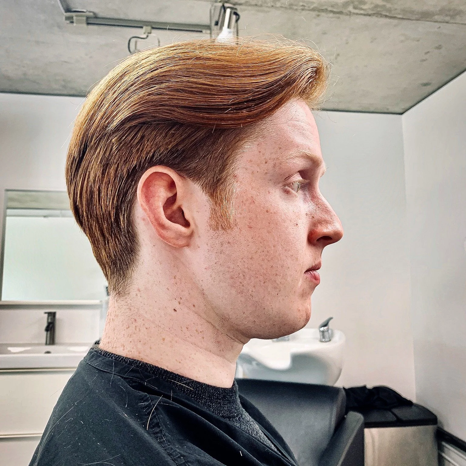 Side profile of a young man with styled, reddish-brown hair in a salon or barbershop.