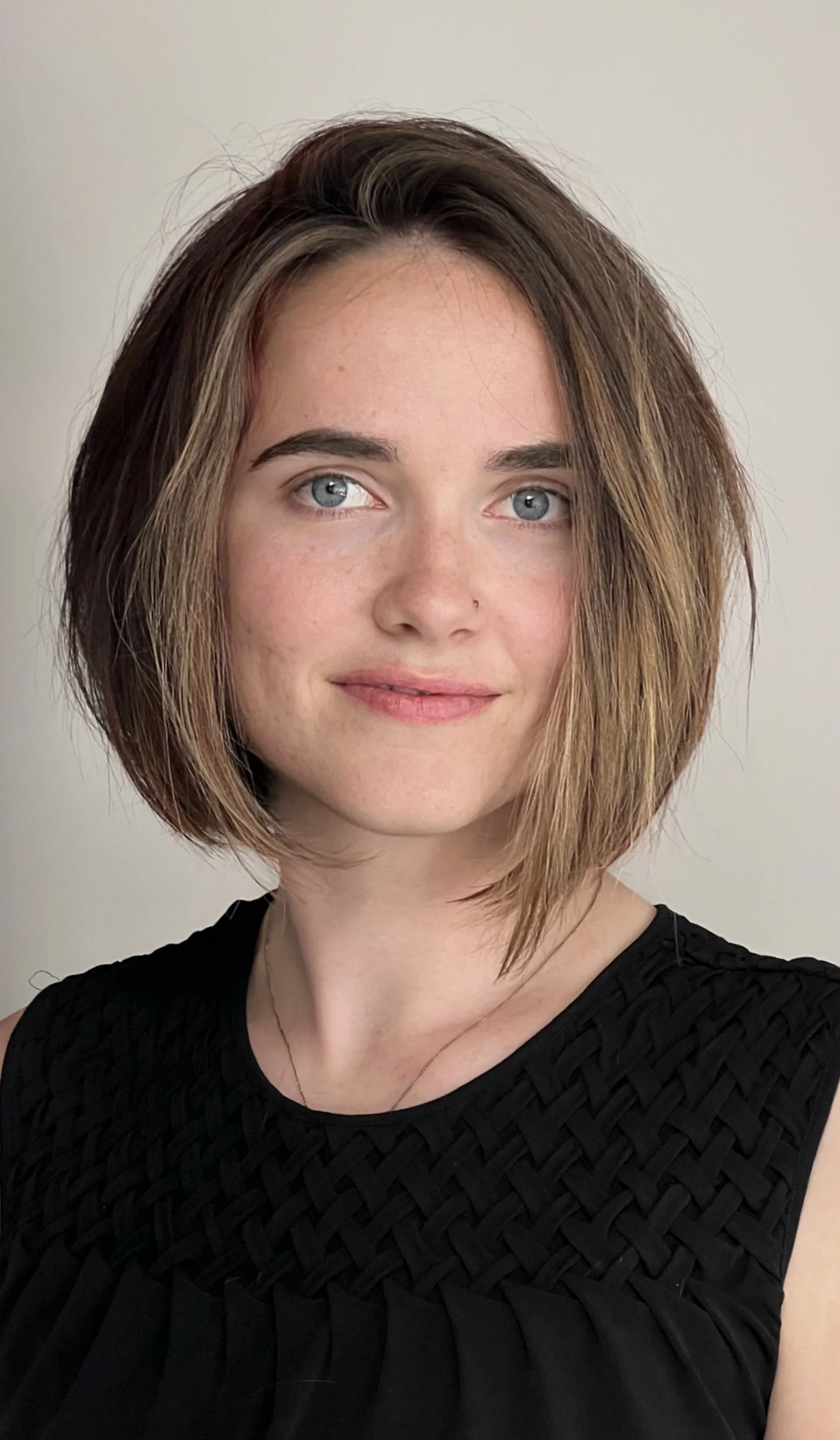 Person with short brown hair, wearing a black top, smiling gently against a neutral background.