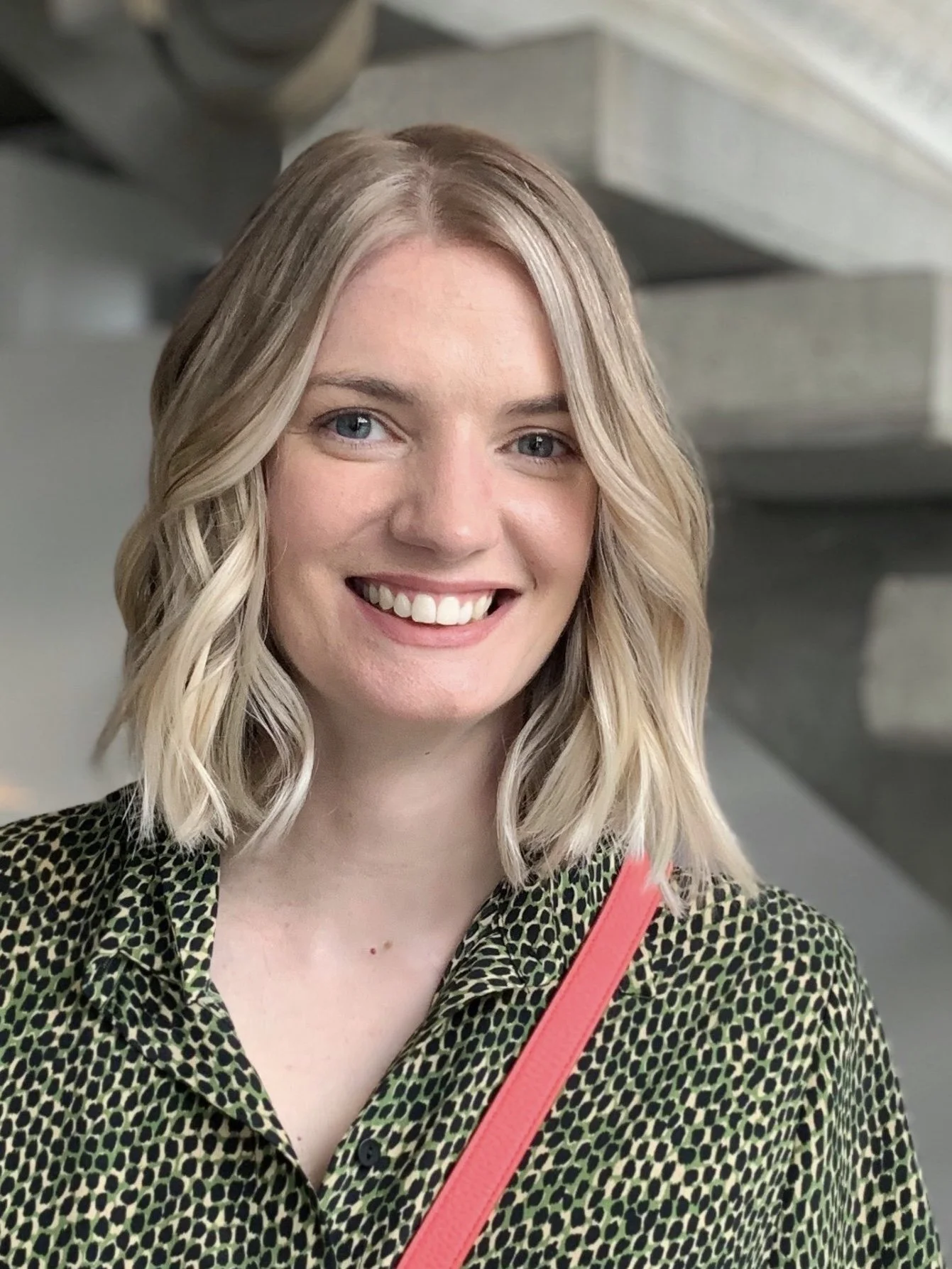 Smiling person with blonde hair wearing a leopard print top and a strap across the shoulder.