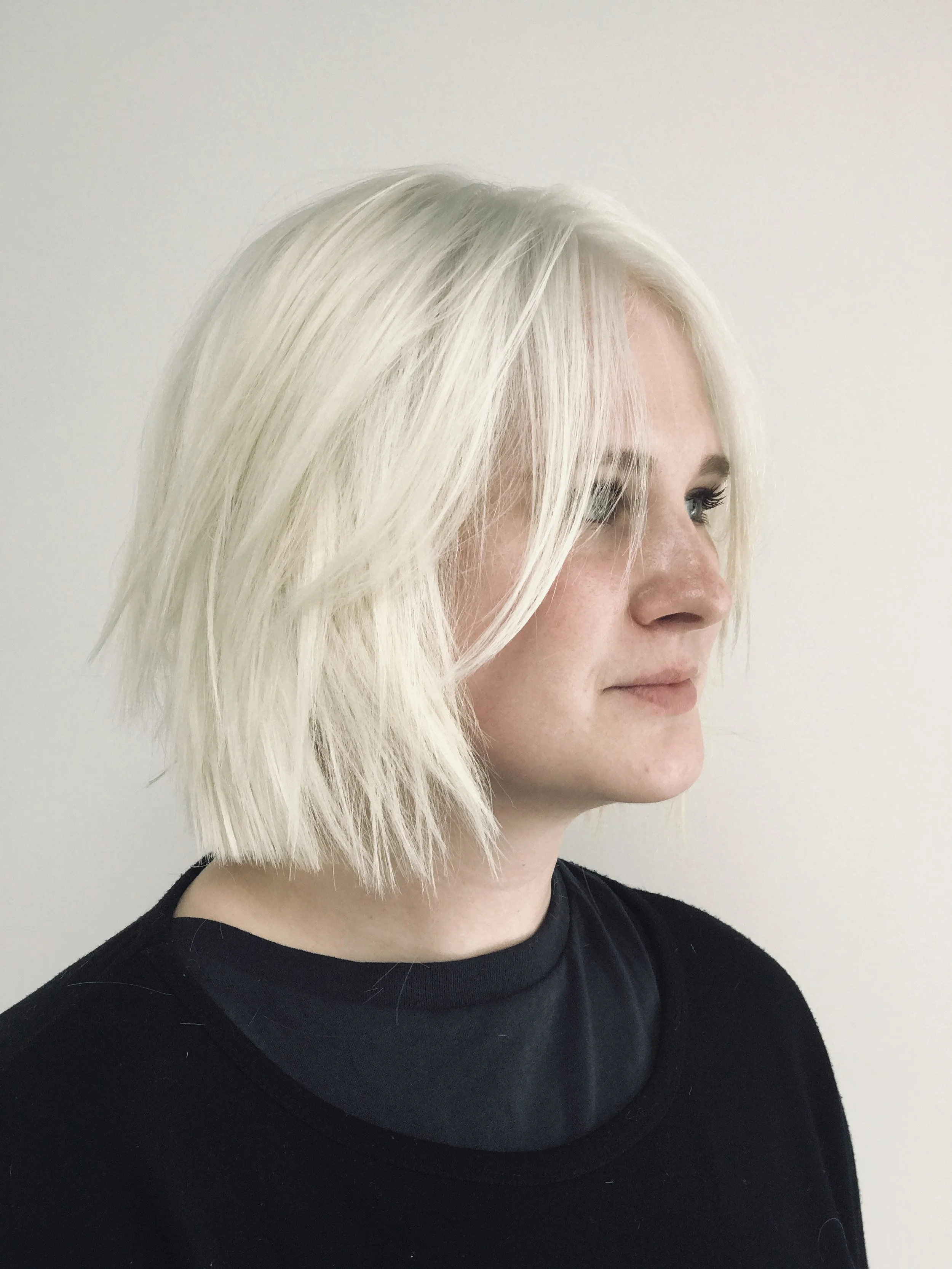 Side view of a person with short, layered blonde hair and black sweater, looking to the right.