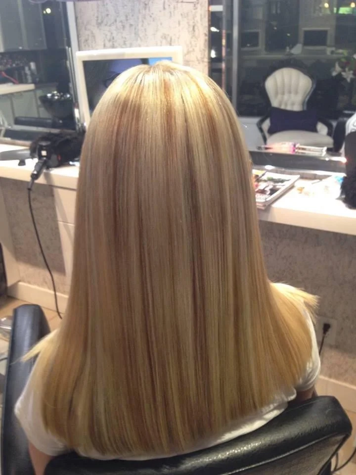 Back of a woman with straight, blonde hair sitting in a salon chair.