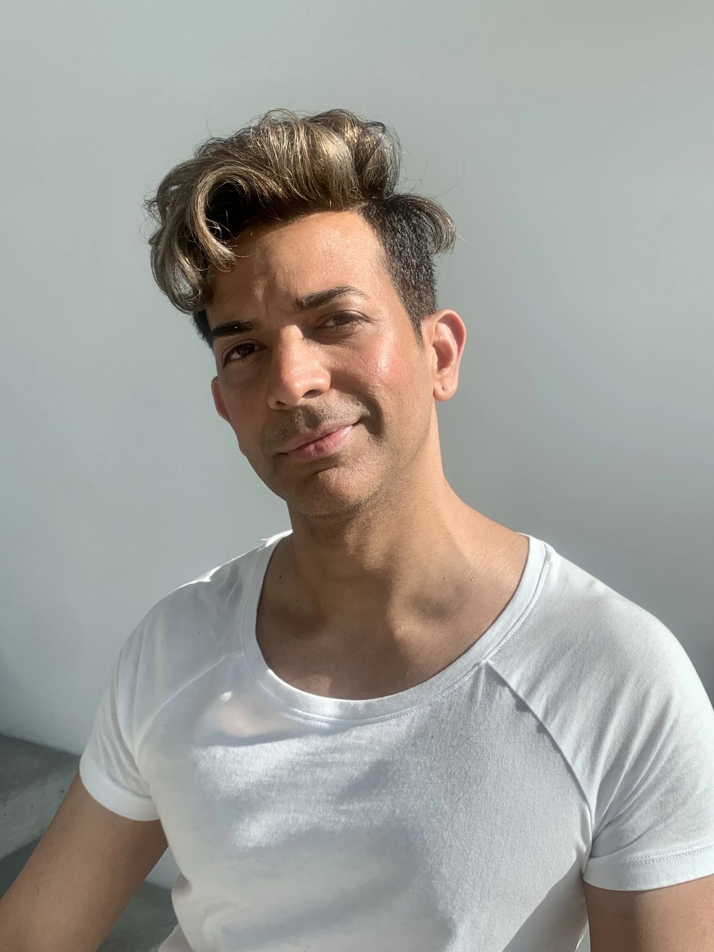 Person with styled hair wearing a white T-shirt, smiling at the camera.