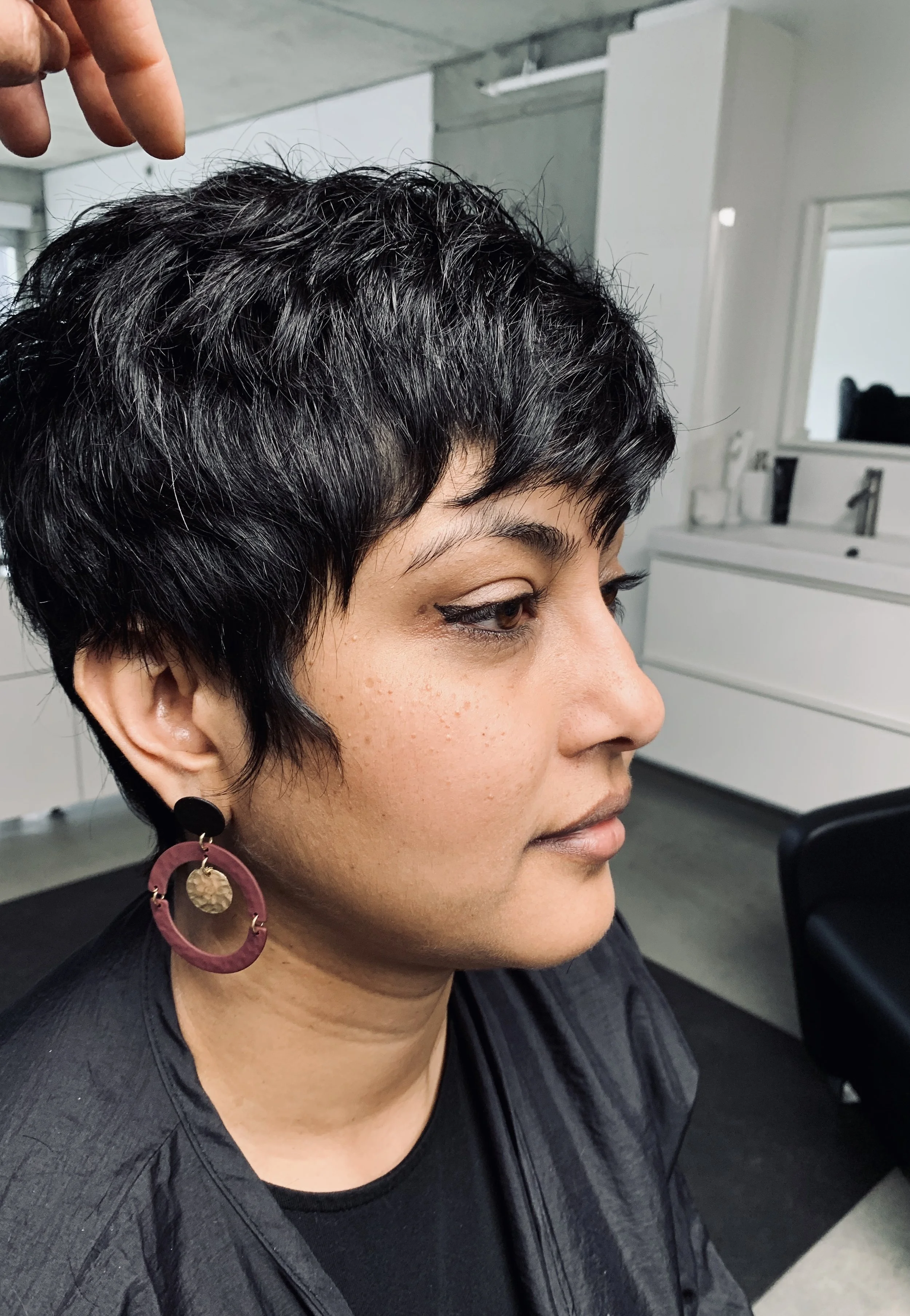 Person with short black hair wearing a large earring in a salon setting