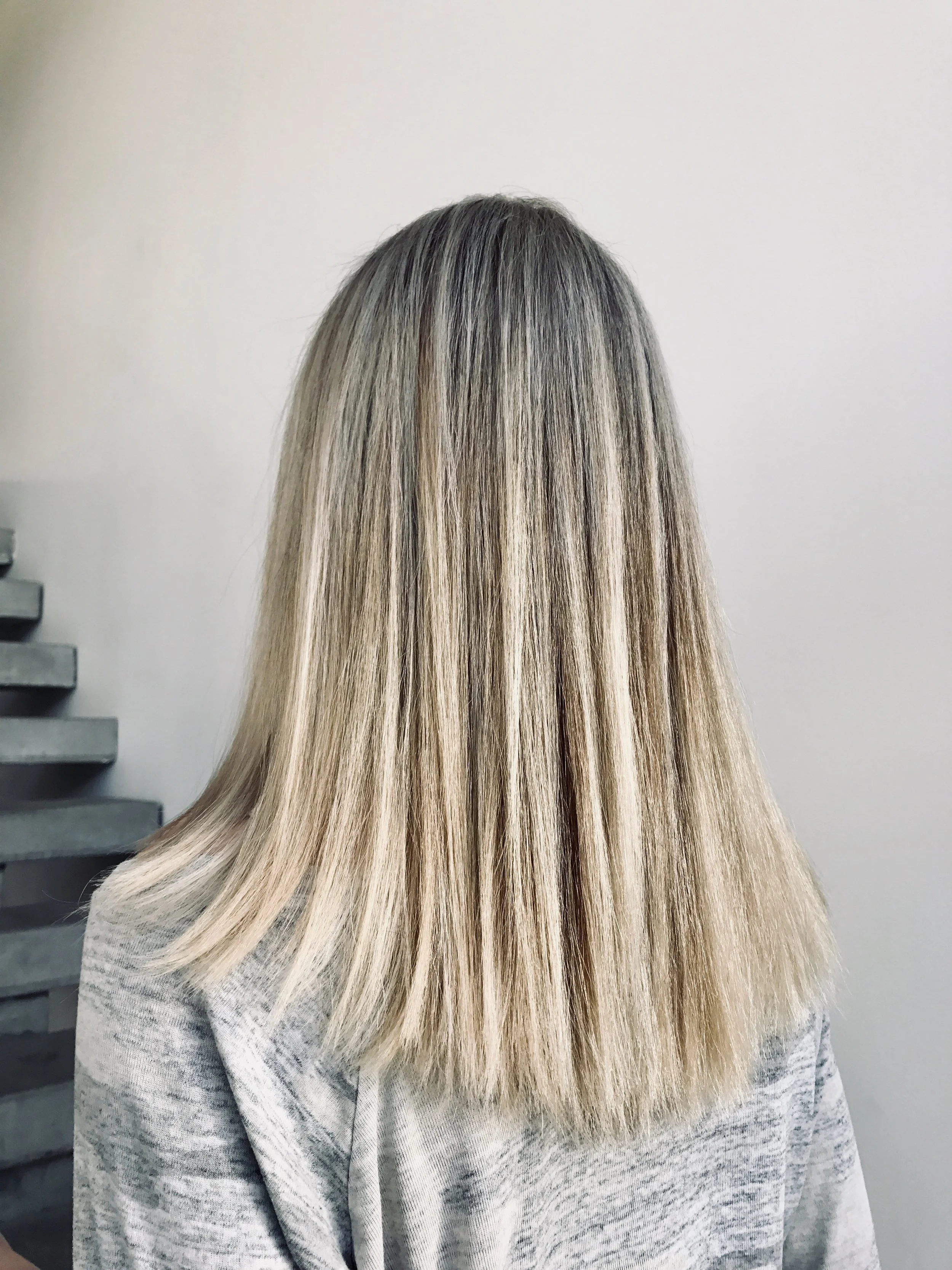 Back of woman's head showing straight, shoulder-length blonde hair with darker roots