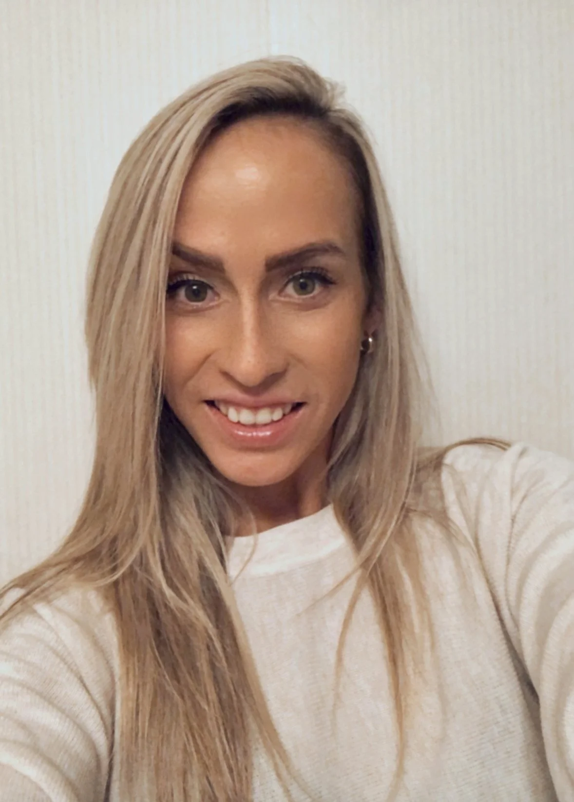 Person with long blond hair smiling, wearing a white shirt.