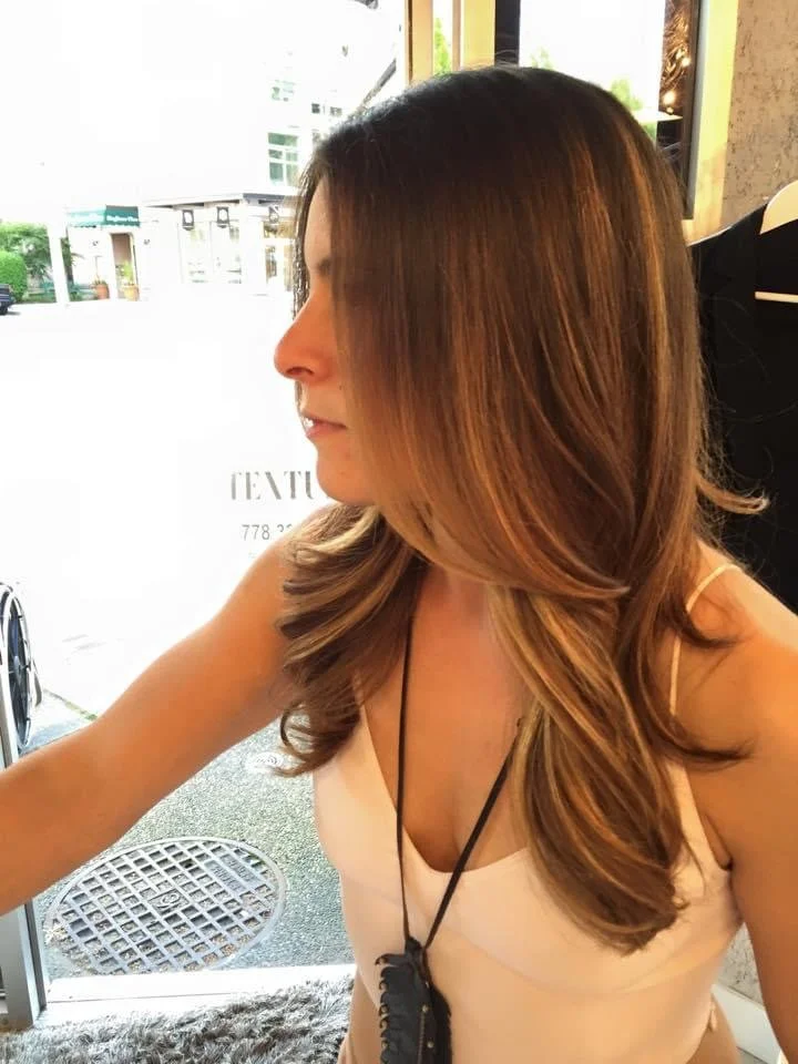 Profile of a woman with long, styled brown hair sitting in a cafe or restaurant.
