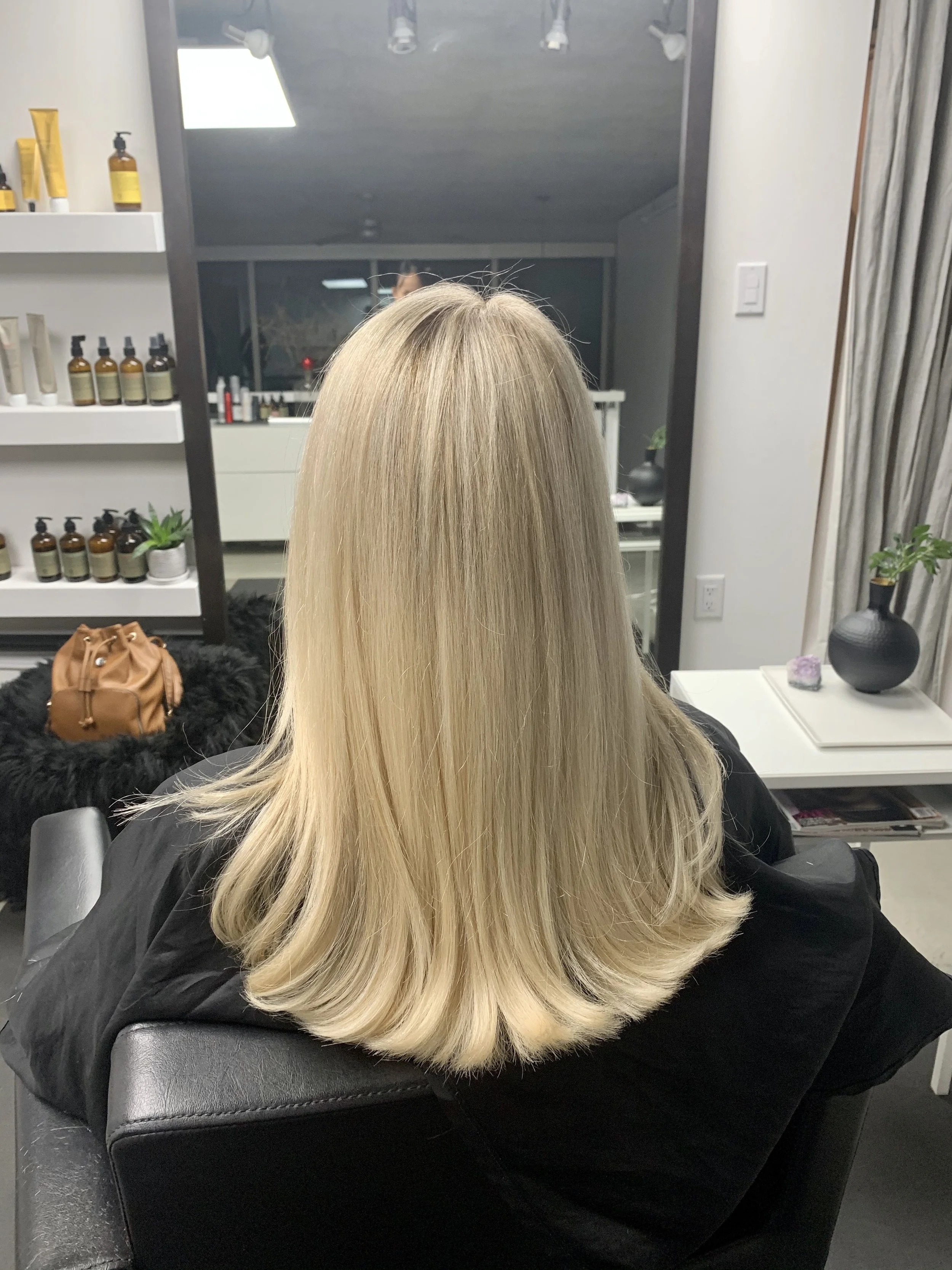 Back of a woman with long, smooth, blonde hair sitting in a salon chair.