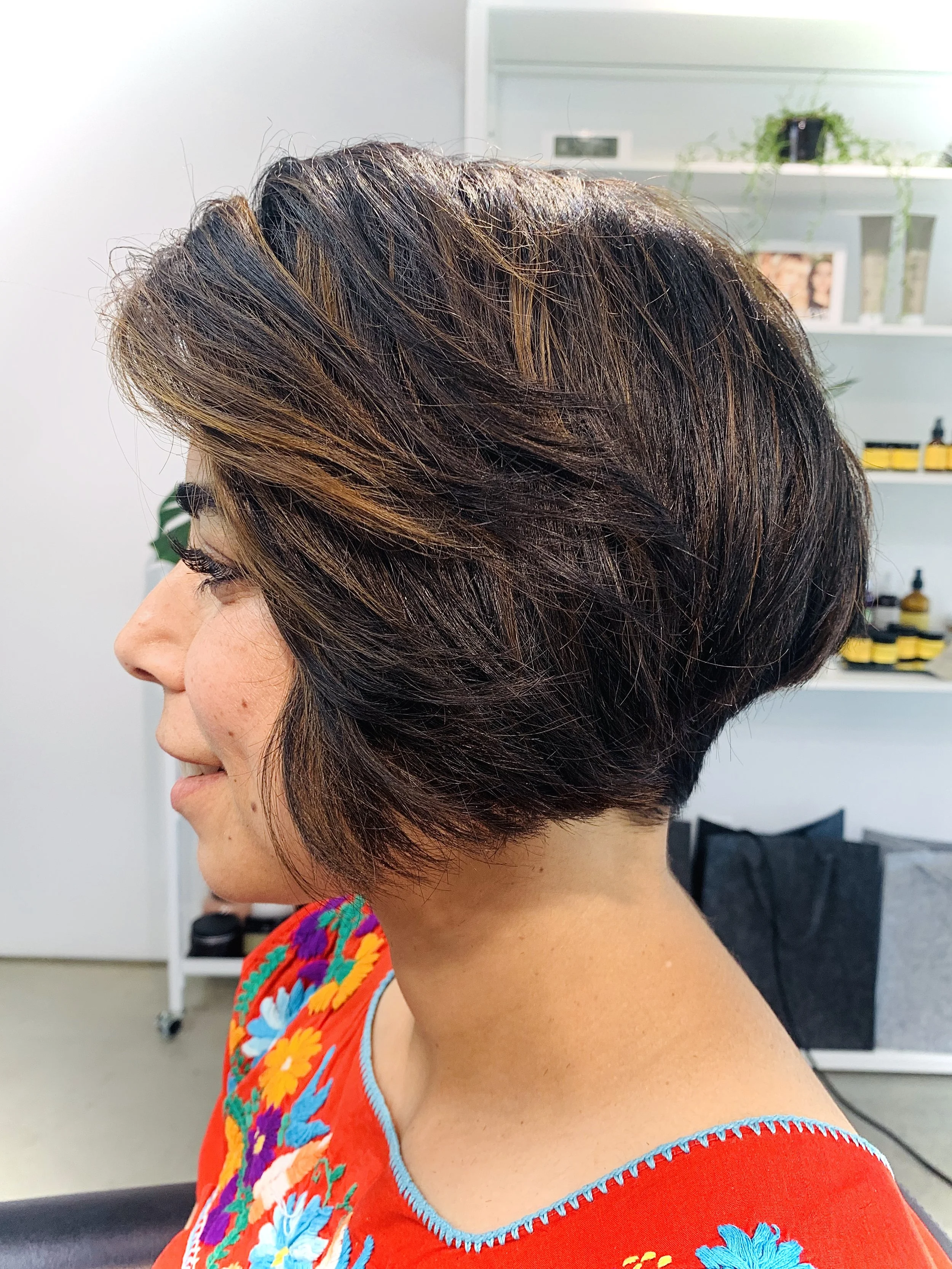 Side profile of a person with a short layered haircut and highlights wearing an embroidered top.