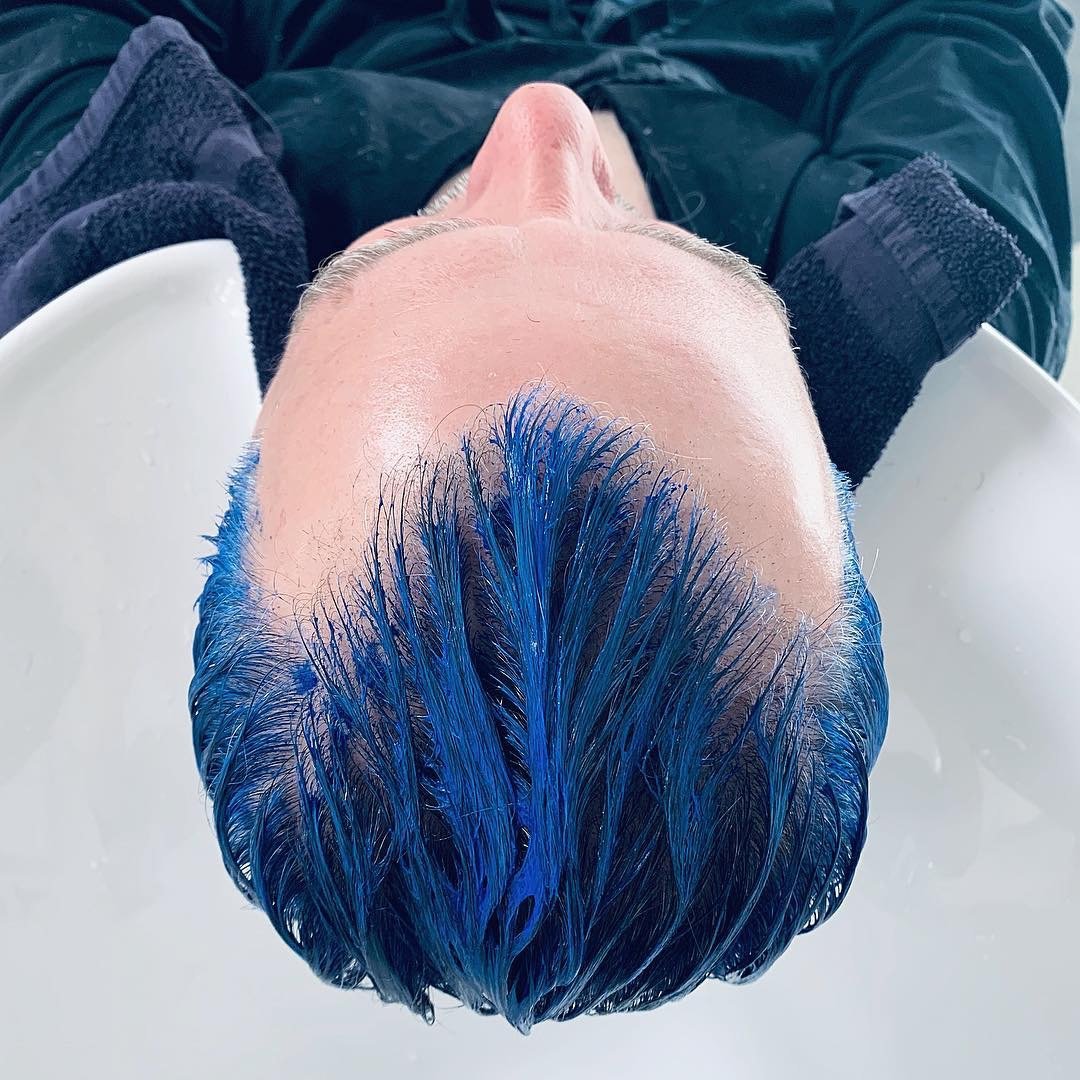 Person with blue hair leaning back over a salon sink, possibly having their hair rinsed.
